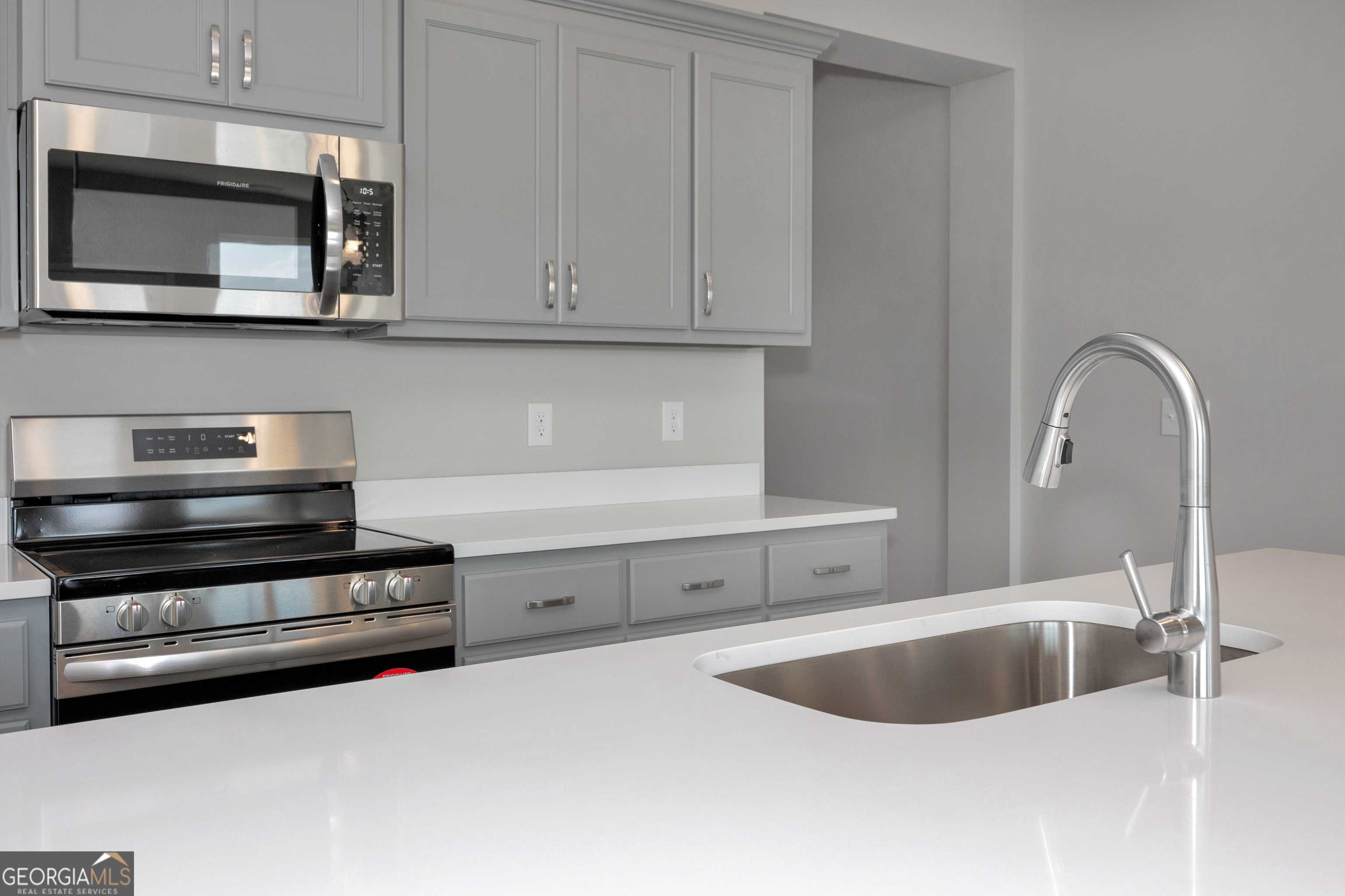 Modern kitchen featuring gray shaker cabinets, stainless steel appliances, and white quartz countertops in Evermore Homes The Luna, Perry, Georgia