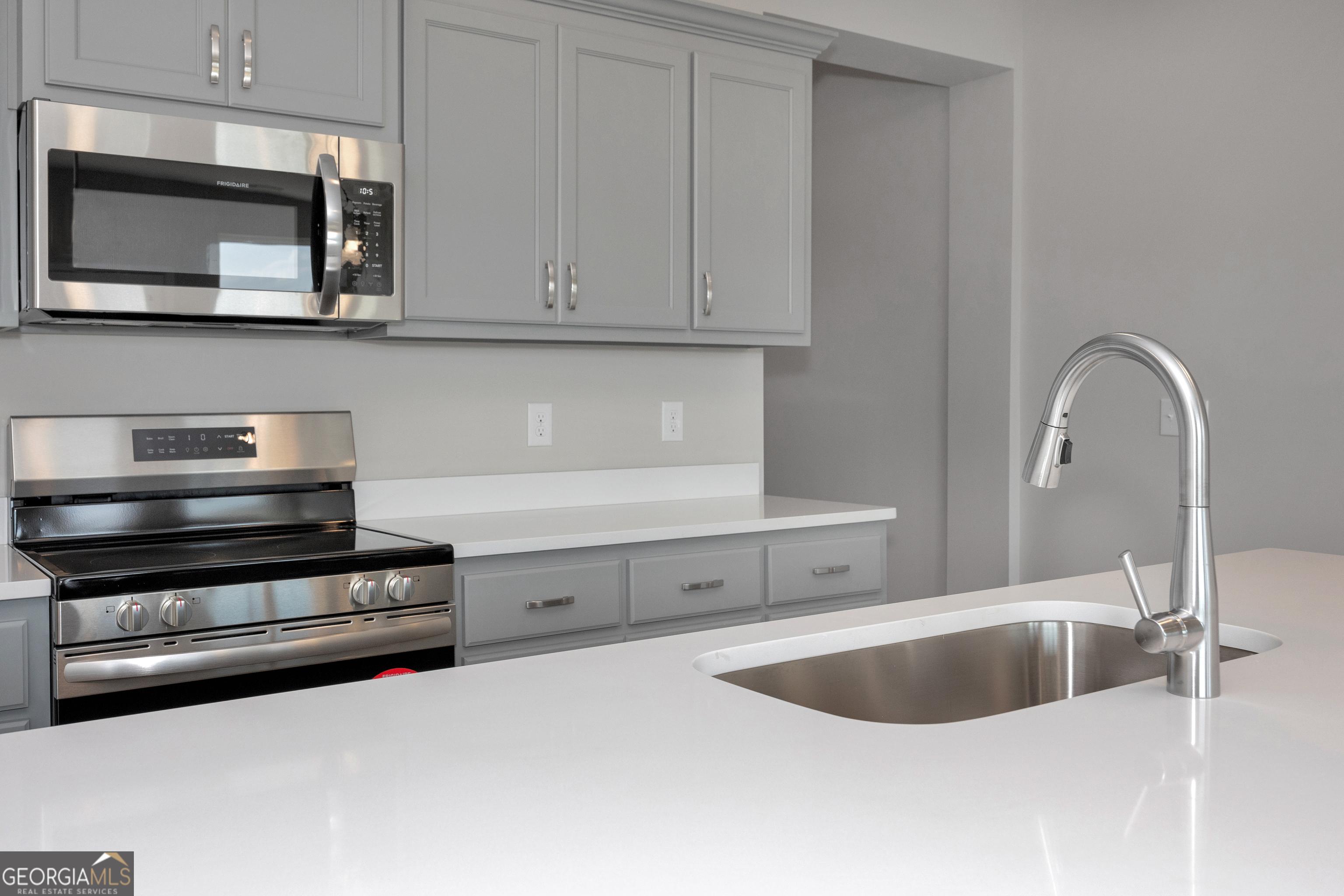 Modern kitchen featuring gray shaker cabinets, stainless steel range and microwave, white quartz counters in The Luna by Evermore Homes, Perry, GA