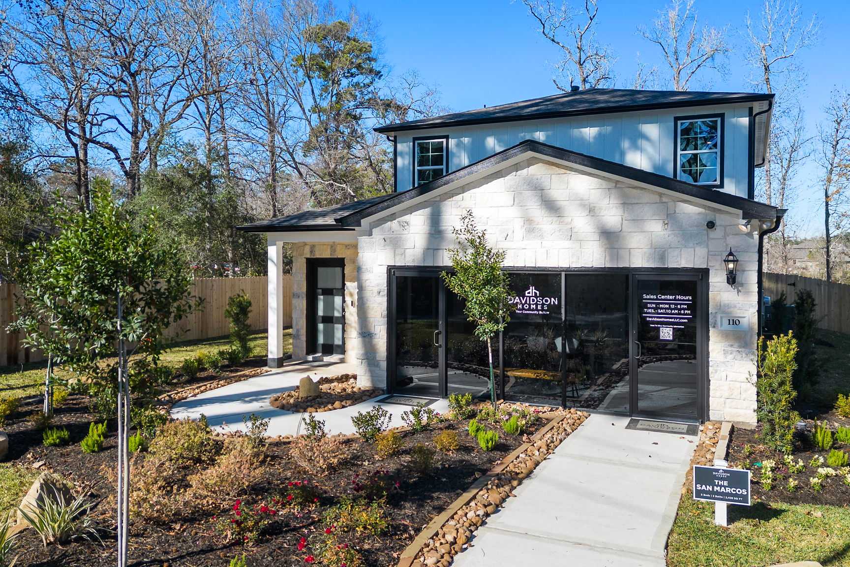 Modern Davidson Homes model at The Lakes at Black Oak in Magnolia, Texas featuring white brick exterior, black trim, large glass entry and landscaped pathway
