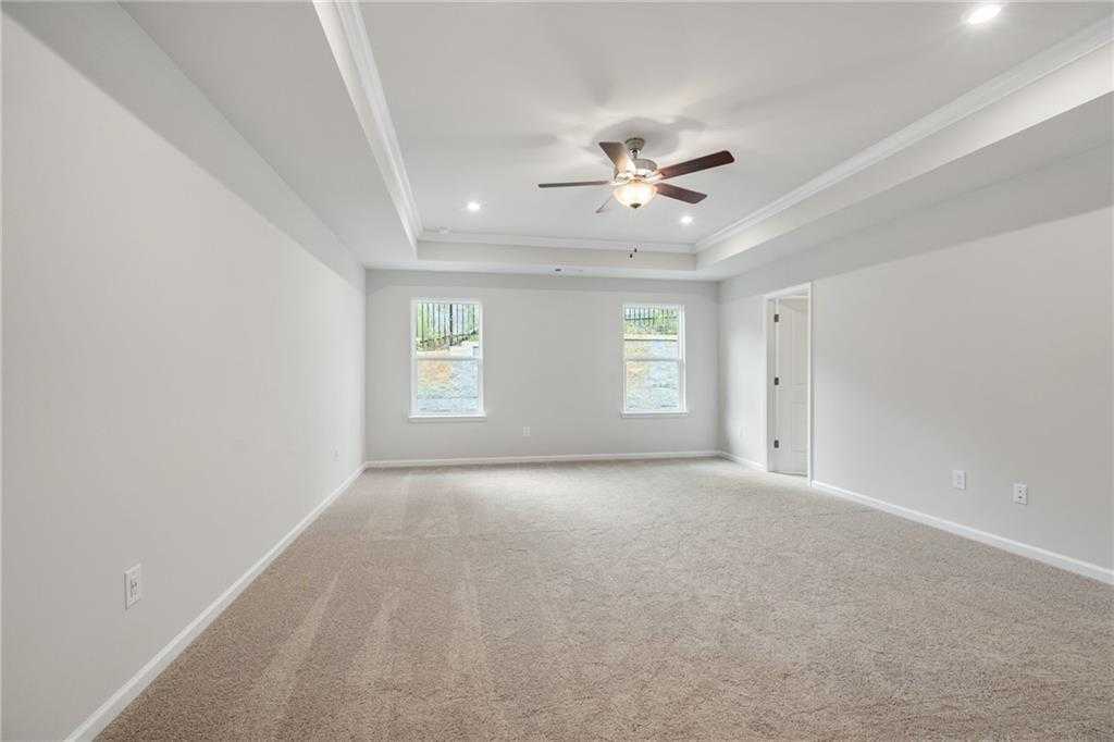 Spacious bedroom with tray ceiling, dual fans, large windows, and beige carpet in Davidson Homes The Cary A, Kennesaw, Georgia
