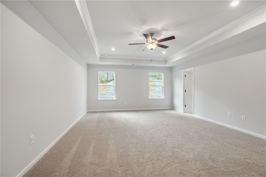 Spacious empty bedroom with beige carpet, tray ceiling, ceiling fan, large windows, and neutral walls in Davidson Homes The Cary A, Kennesaw, GA