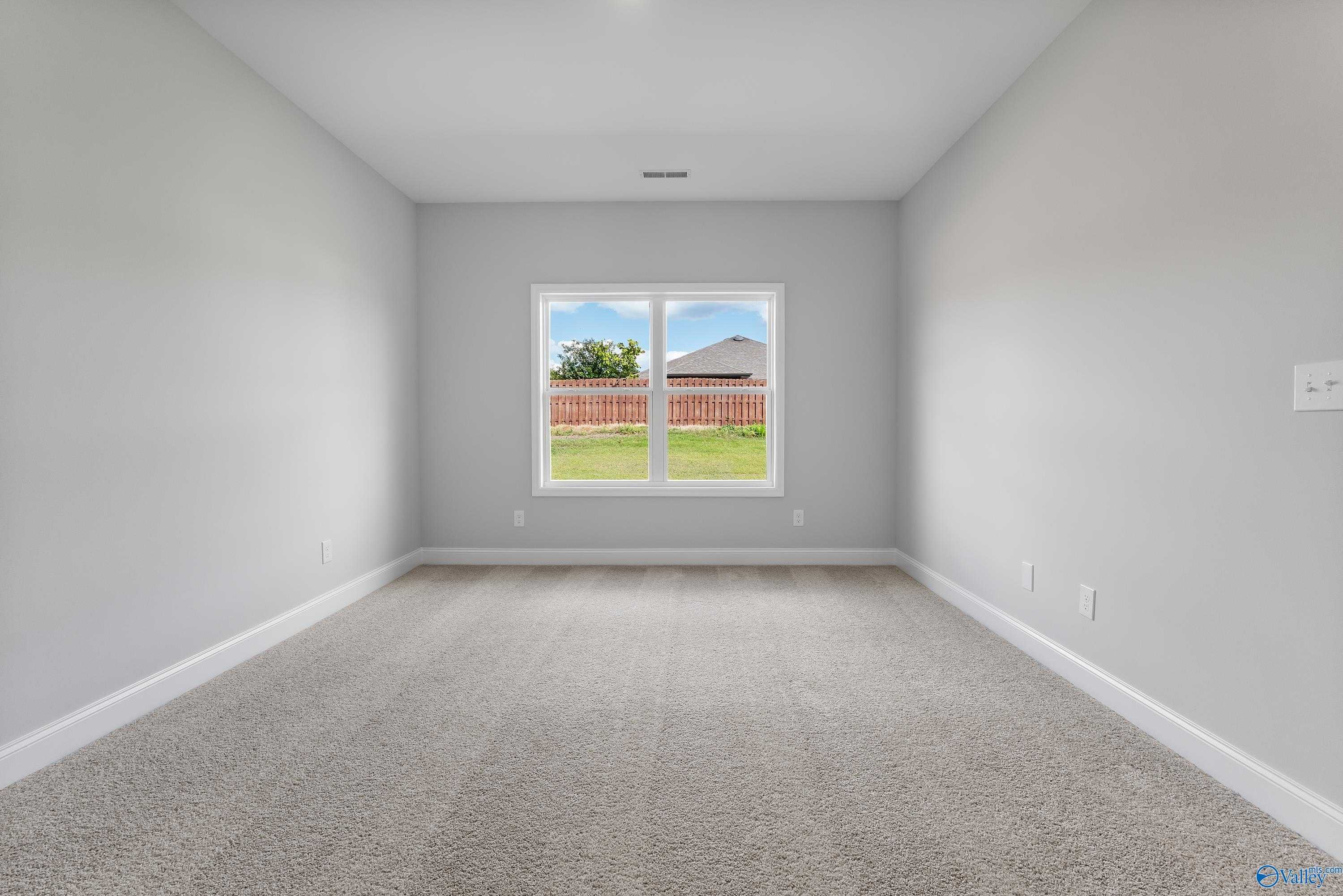 Empty bedroom with gray walls, beige carpet, and dual windows to fenced backyard in Davidson Homes The Franklin C, Toney, AL