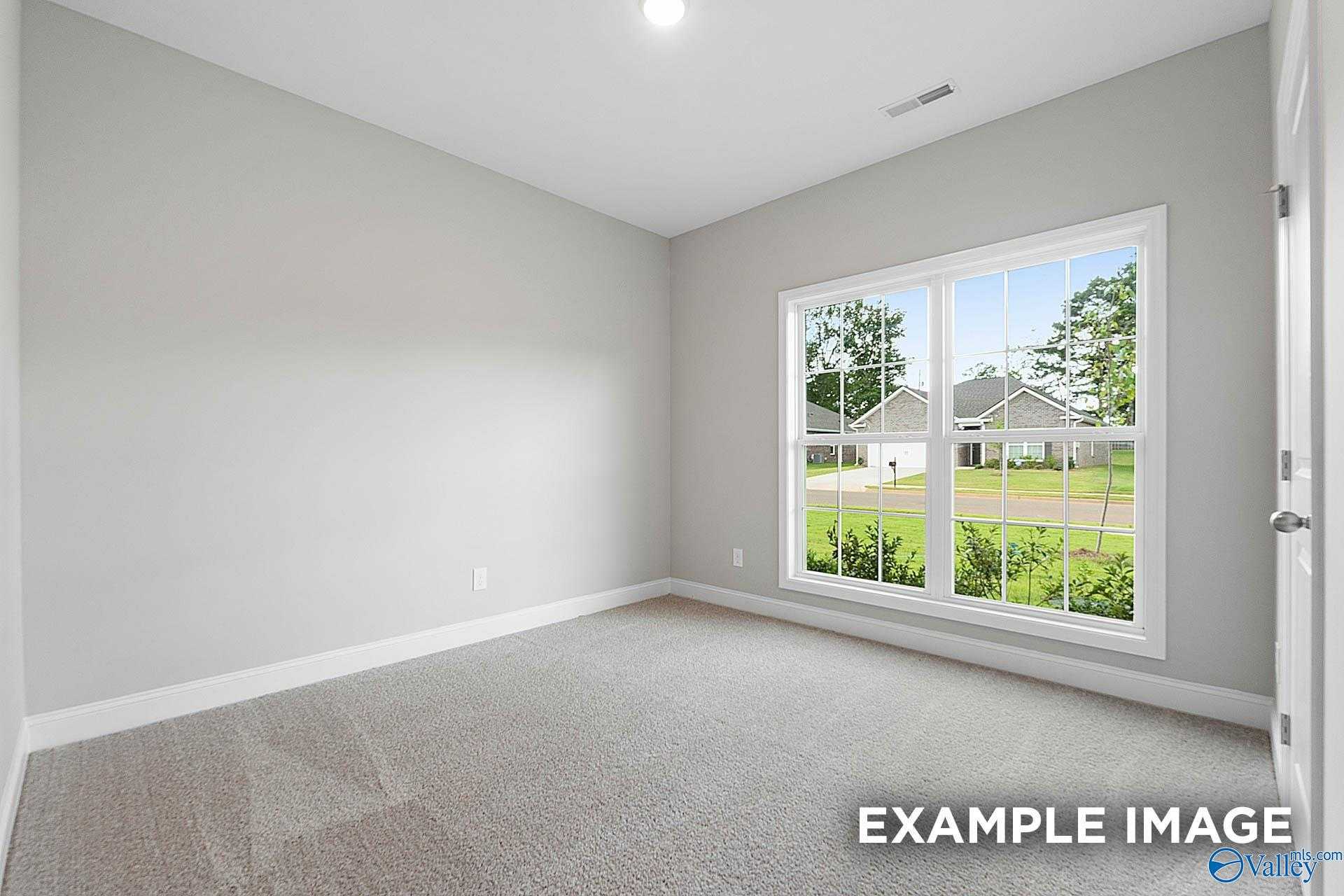 Bright empty bedroom with gray walls, large window overlooking green yard and neighborhood in Davidson Homes The Franklin E, Hazel Green, Alabama