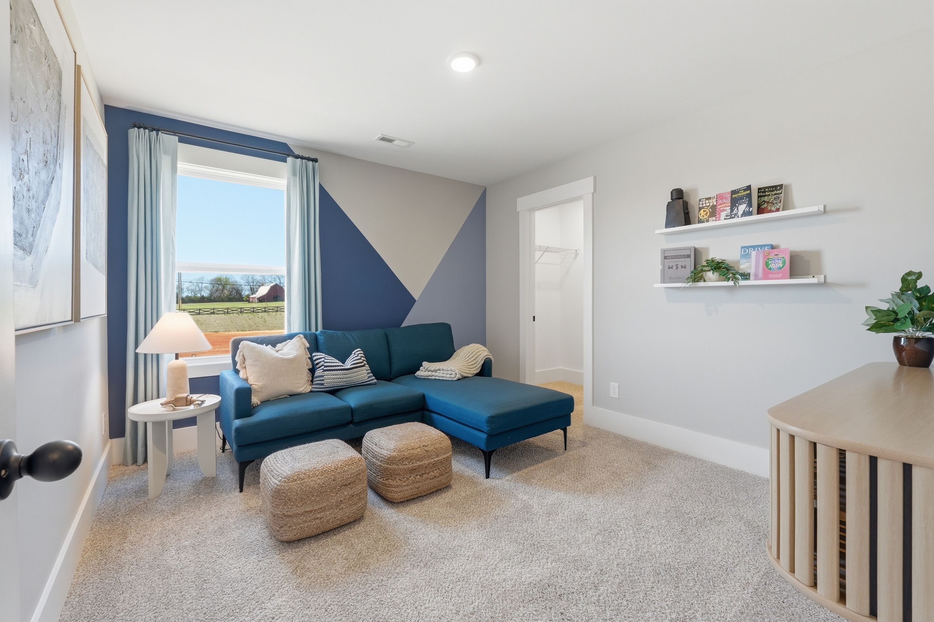 Cozy bonus room at Berry Cove in New Market Alabama with navy blue L-shaped sofa, geometric accent wall, and window overlooking fields