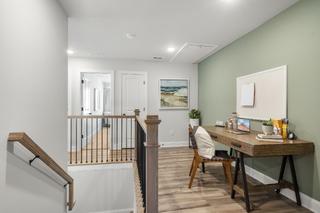 Spacious upper floor home office in Washington H townhome with wooden desk, laptop, green accent wall, and railing overlook