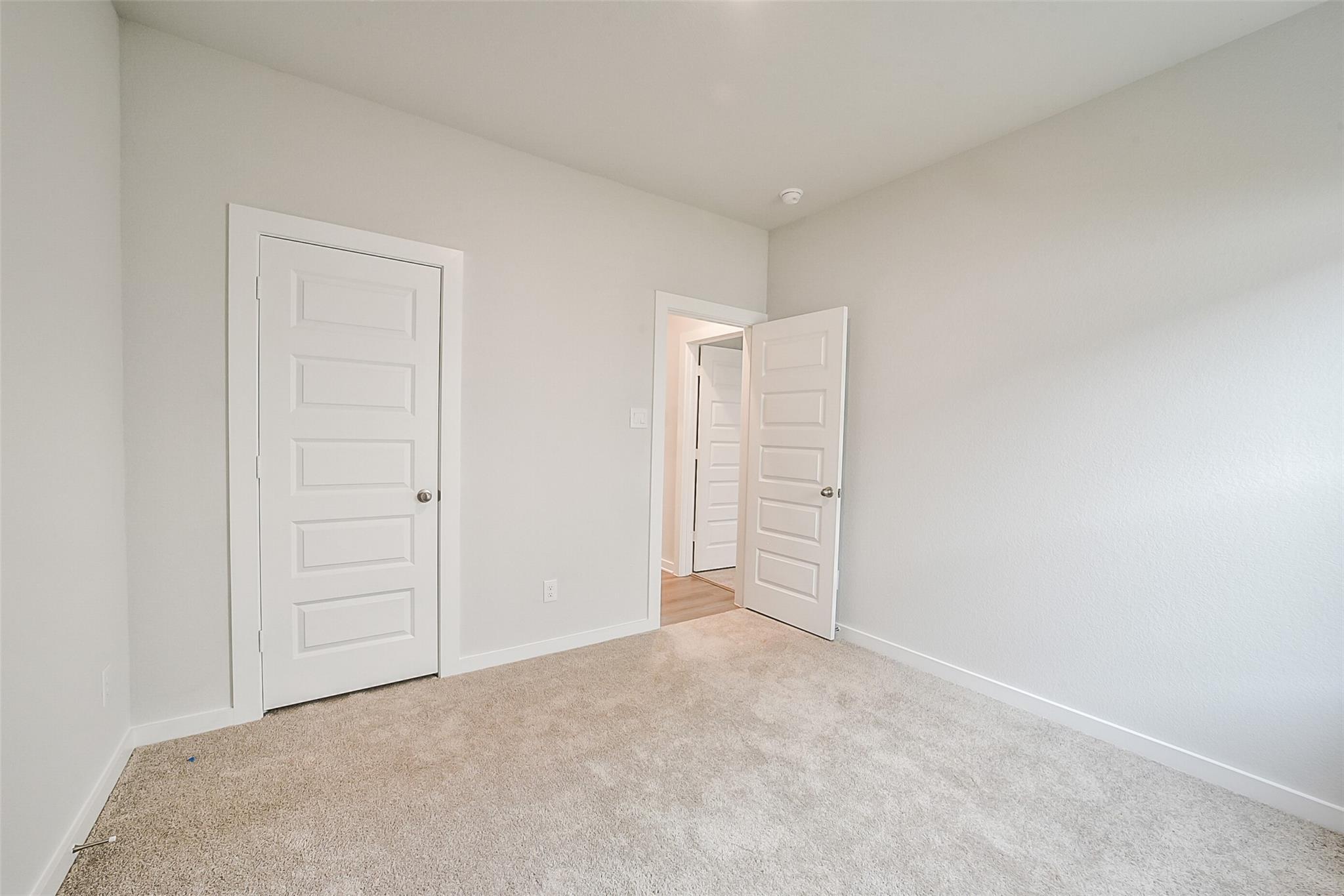 Bright secondary bedroom with gray walls, beige carpet, and open en-suite bathroom doors in Davidson Homes The Frio F, Conroe, Texas