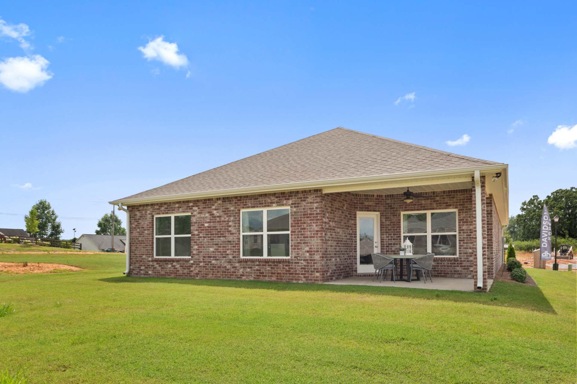 Single-story brick home with covered porch, patio seating under umbrella, and lush green lawn at Flint Meadows in New Market, Alabama