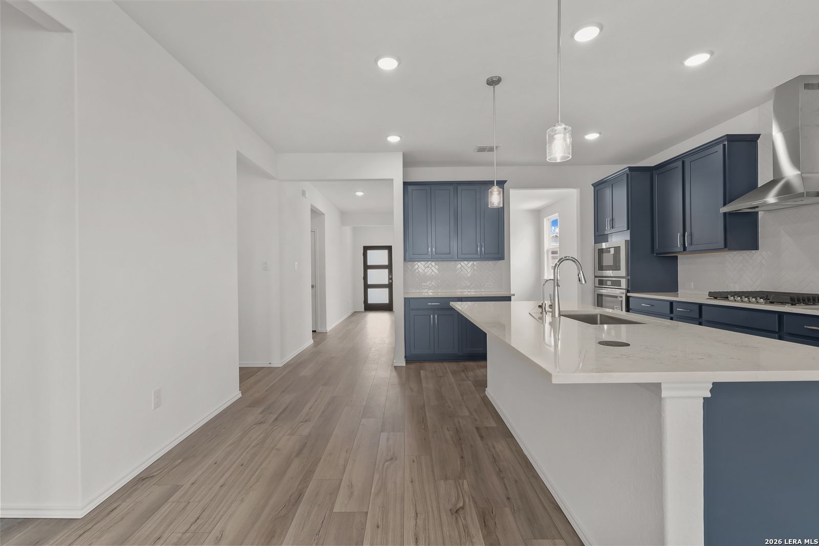 Open-concept kitchen with navy cabinets, white quartz island, stainless appliances in The Glenwood E home, Elmendorf, Texas