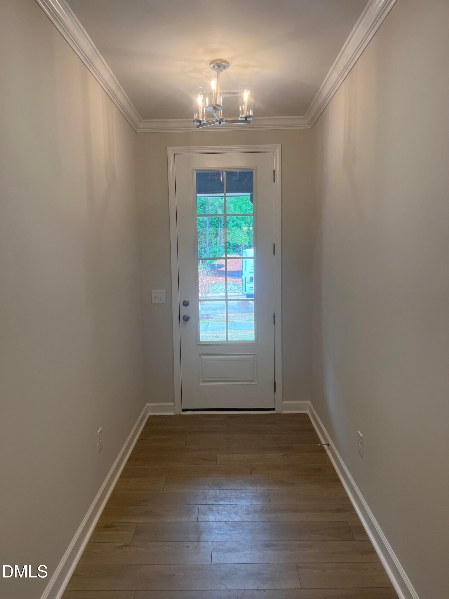 Elegant hallway with beige walls, hardwood floors, chandelier, and glass door to wooded backyard in Davidson Homes Ashport G, Wake Forest NC