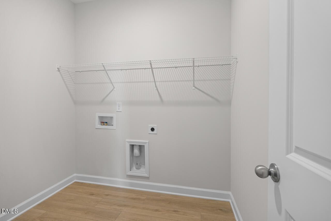 Laundry room with wire shelving, washer connections, and wood-look flooring in Davidson Homes The Daphne D, Woodland Crossing, Zebulon NC