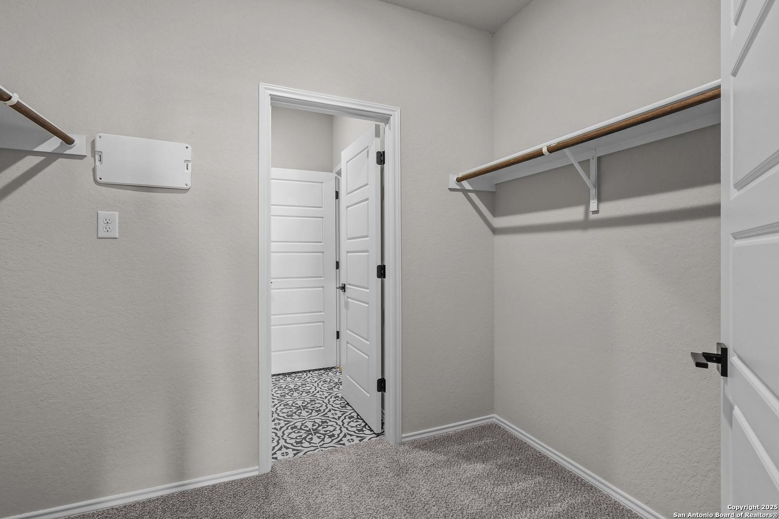 Spacious walk-in master closet with wooden shelving and adjacent bathroom featuring patterned tile in Davidson Homes The Brazos C, San Antonio