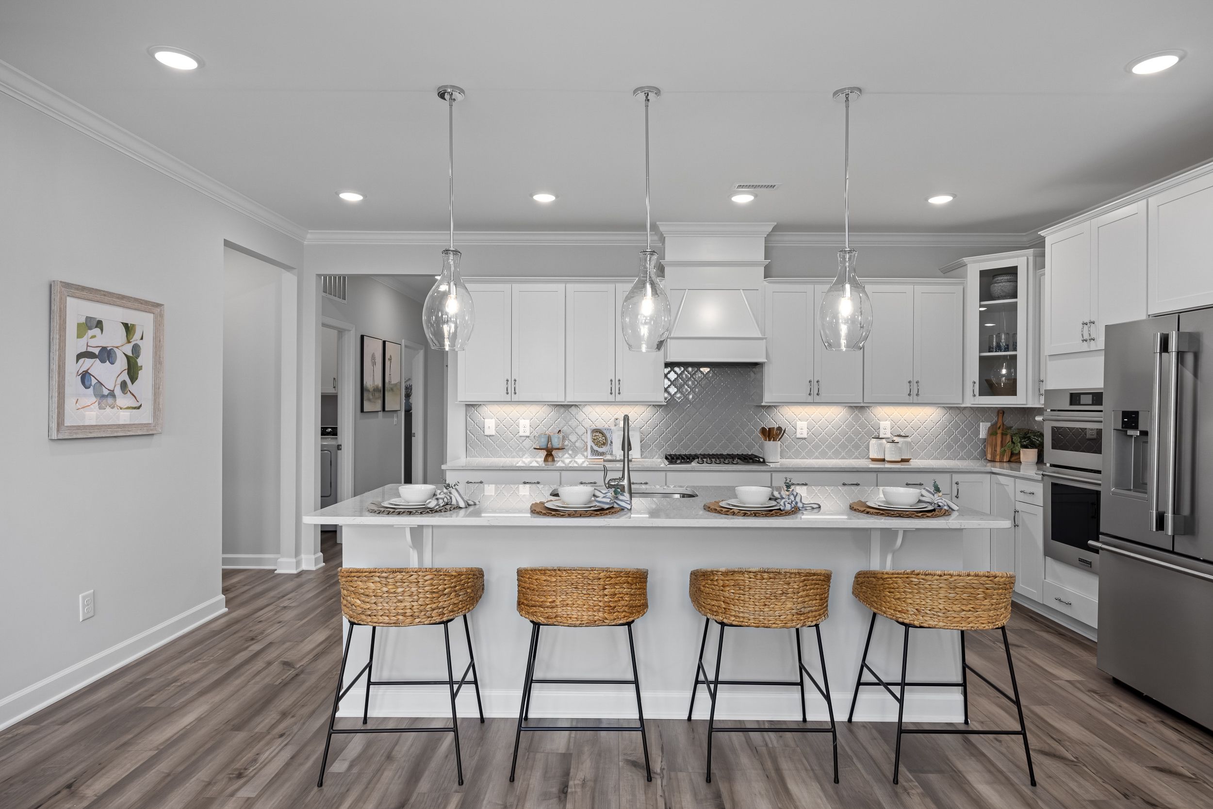 Modern kitchen in The Magnolia A with white shaker cabinets, large island, woven bar stools, stainless appliances, and pendant lights