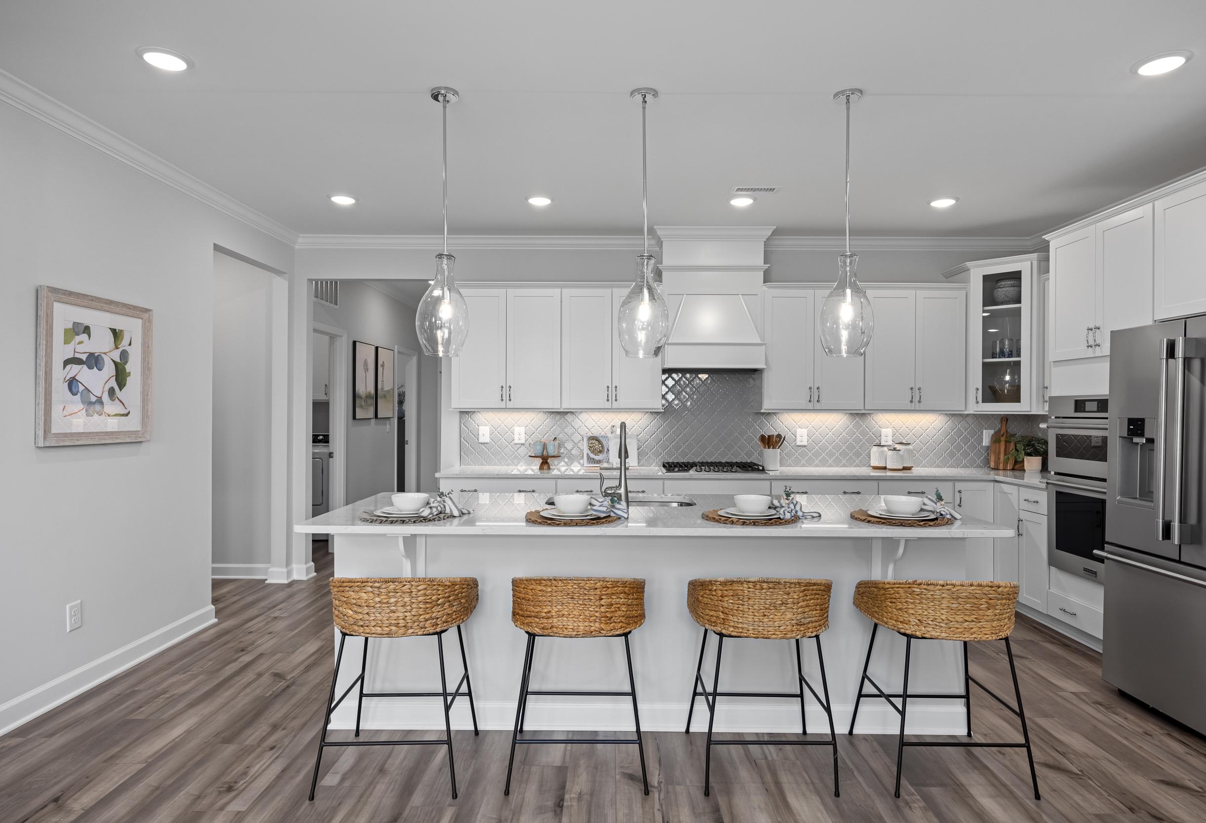 Modern kitchen in The Magnolia A with white shaker cabinets, large island, woven bar stools, stainless appliances, and pendant lights