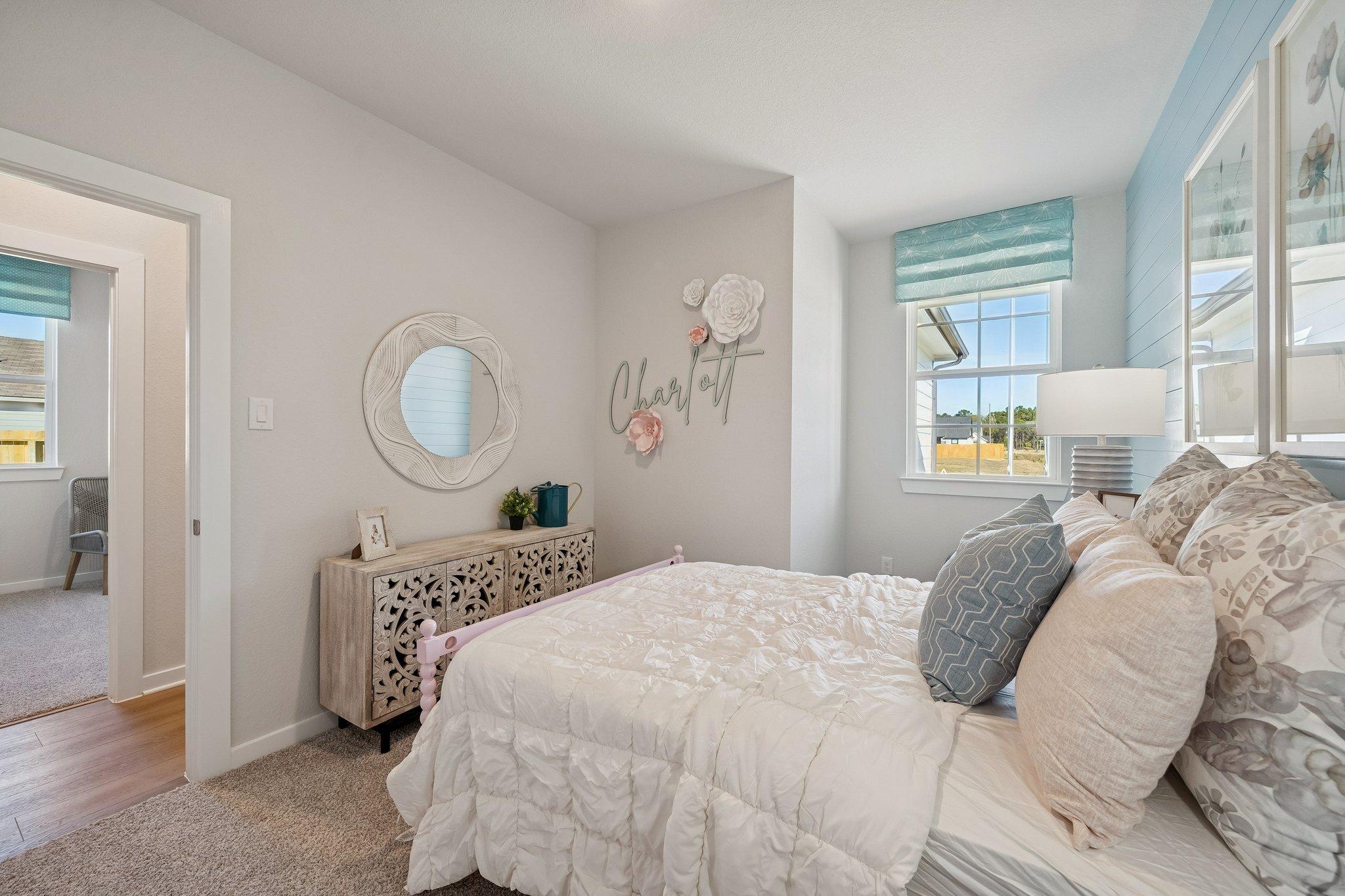 Cozy girl's bedroom at Spring Branch Crossing in Conroe Texas with white bed blue pillows Charlotte wall decor and round mirror