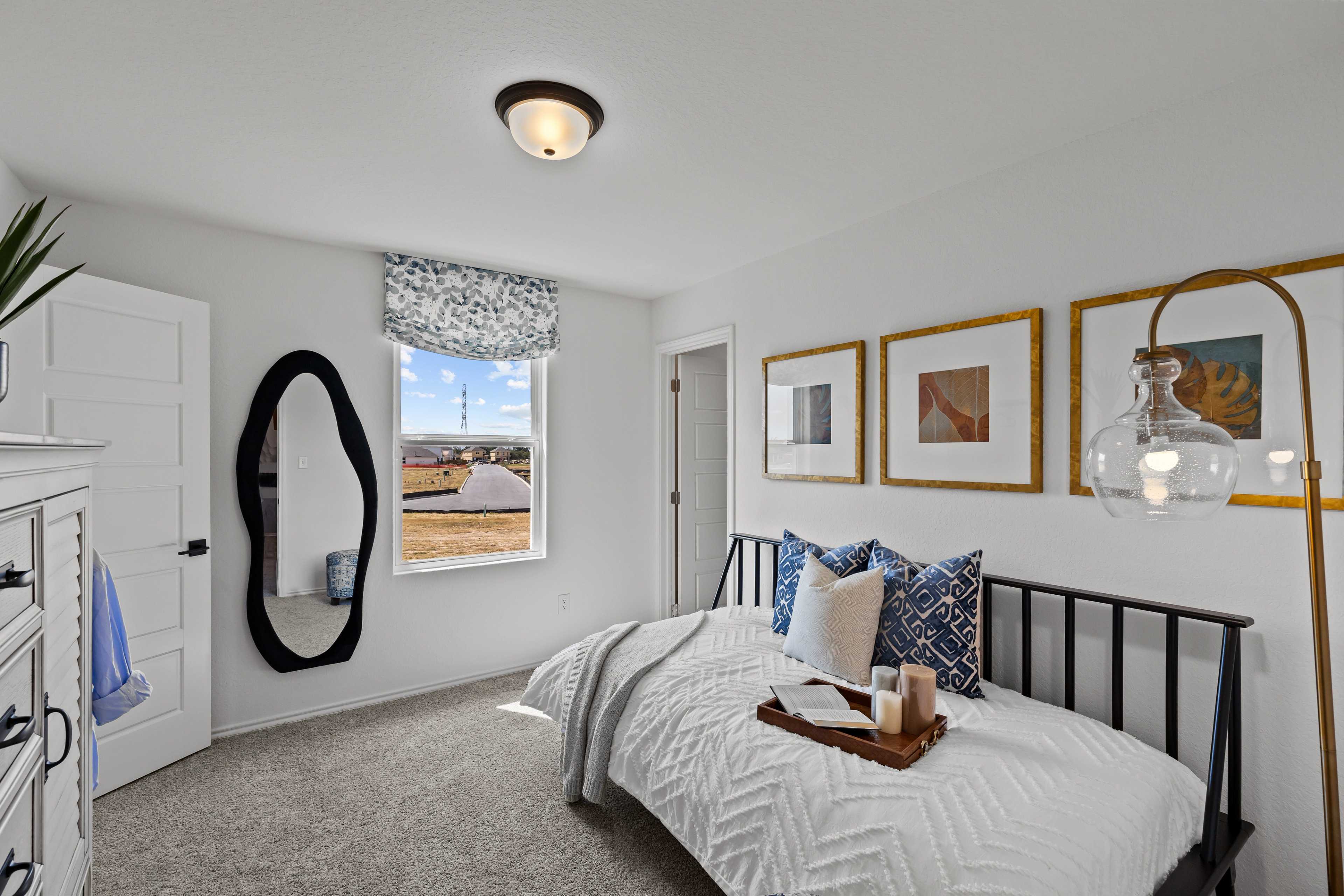 Cozy bedroom at Hickory Ridge in Elmendorf TX by Davidson Homes with twin bed, arched mirror, blue curtains and framed art