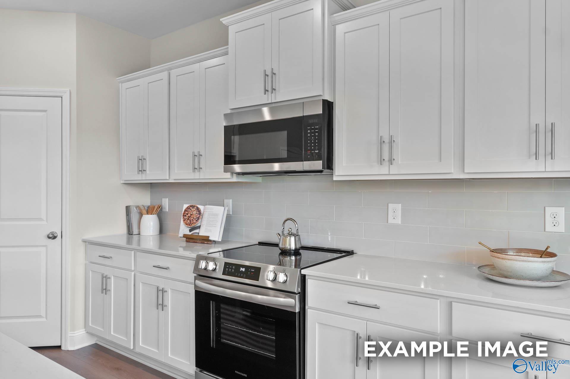 Modern kitchen with white cabinets, quartz countertops, and stainless appliances in The Madison A home, Athens, Alabama.