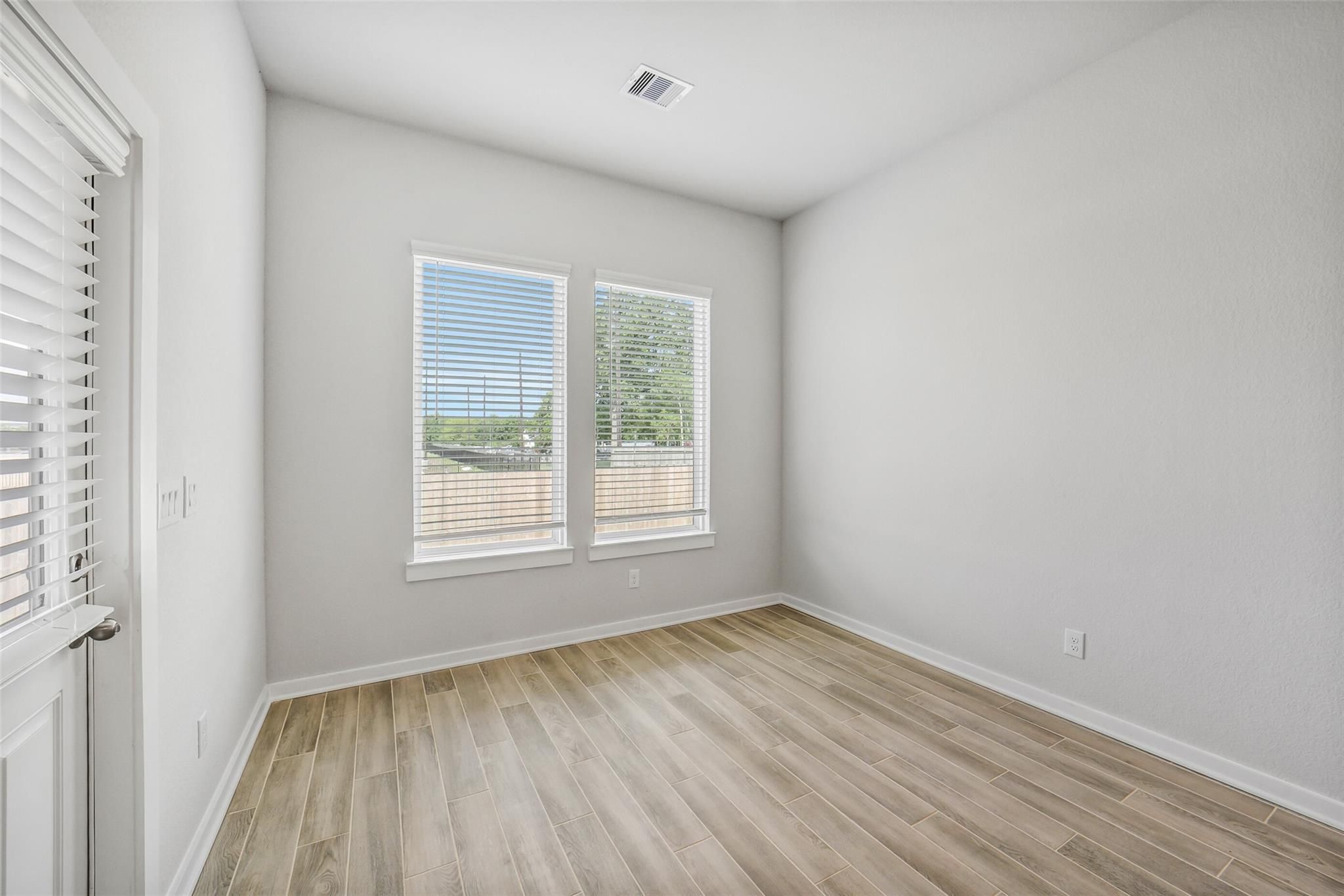 Bright empty bedroom with light gray walls, luxury vinyl plank floors, and double windows overlooking backyard in Davidson Homes The Acadia C, Magnolia, Texas