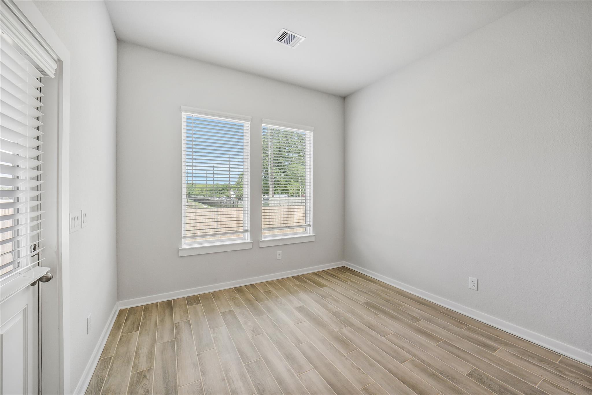 Bright empty bedroom with light gray walls, luxury vinyl plank floors, and double windows overlooking backyard in Davidson Homes The Acadia C, Magnolia, Texas