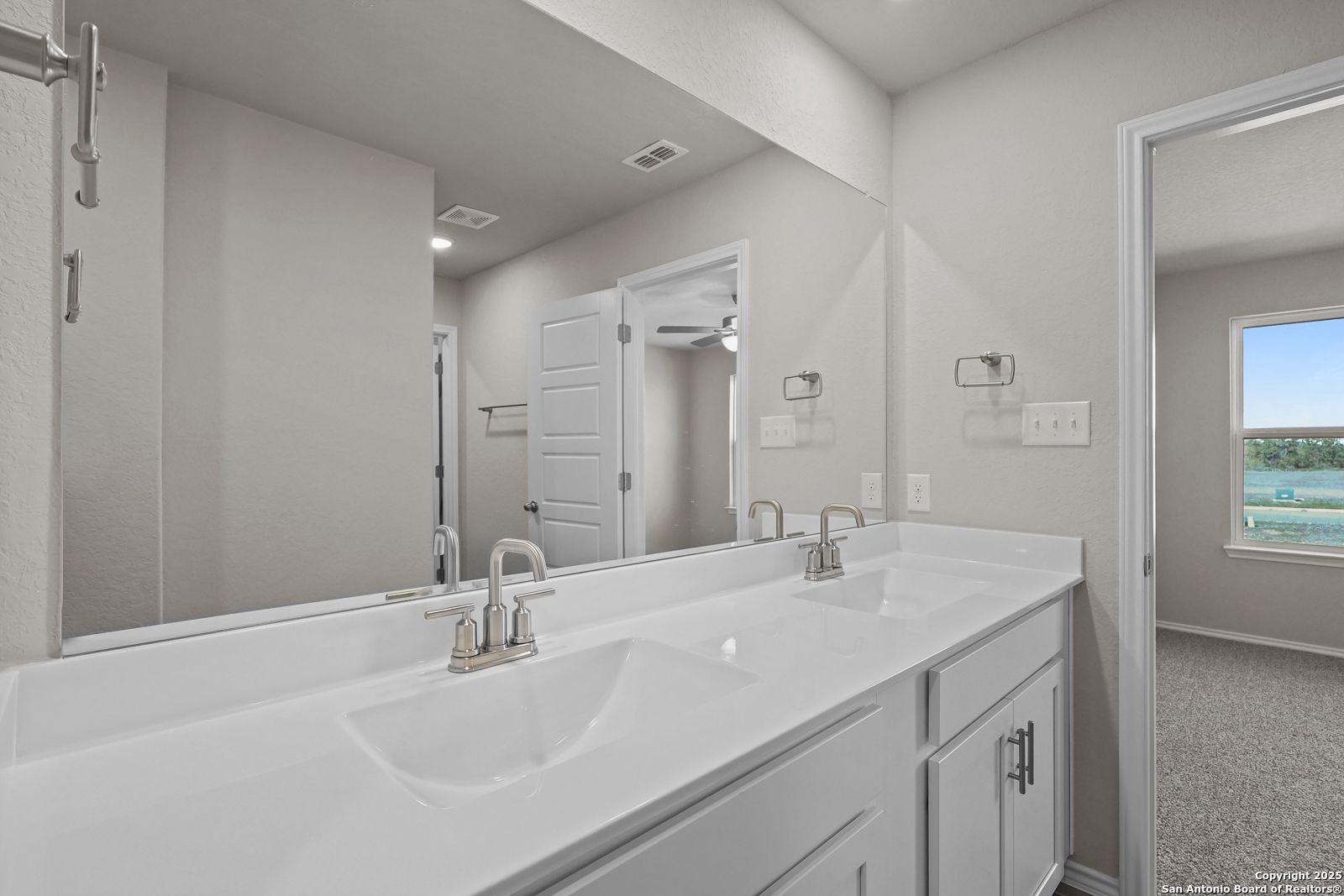 Elegant master bathroom double vanity with white sinks, chrome faucets, and large mirror in Davidson Homes The Trinity D, San Antonio, Texas