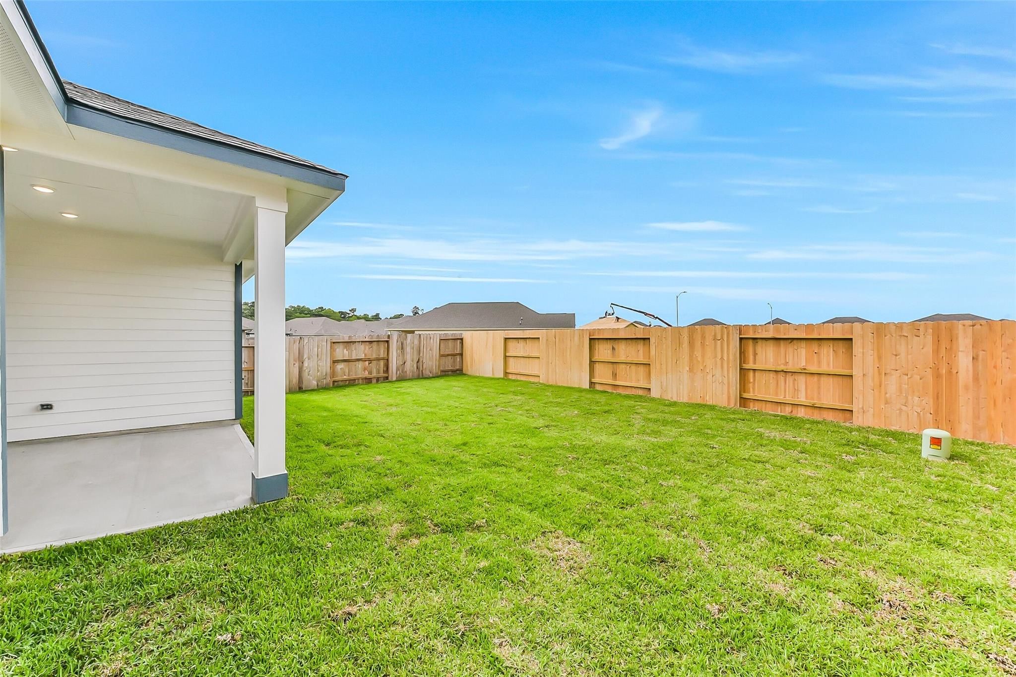 Covered back patio and lush green backyard with wooden privacy fence in Davidson Homes The Sequoia C, Sundance Cove, Crosby, Texas