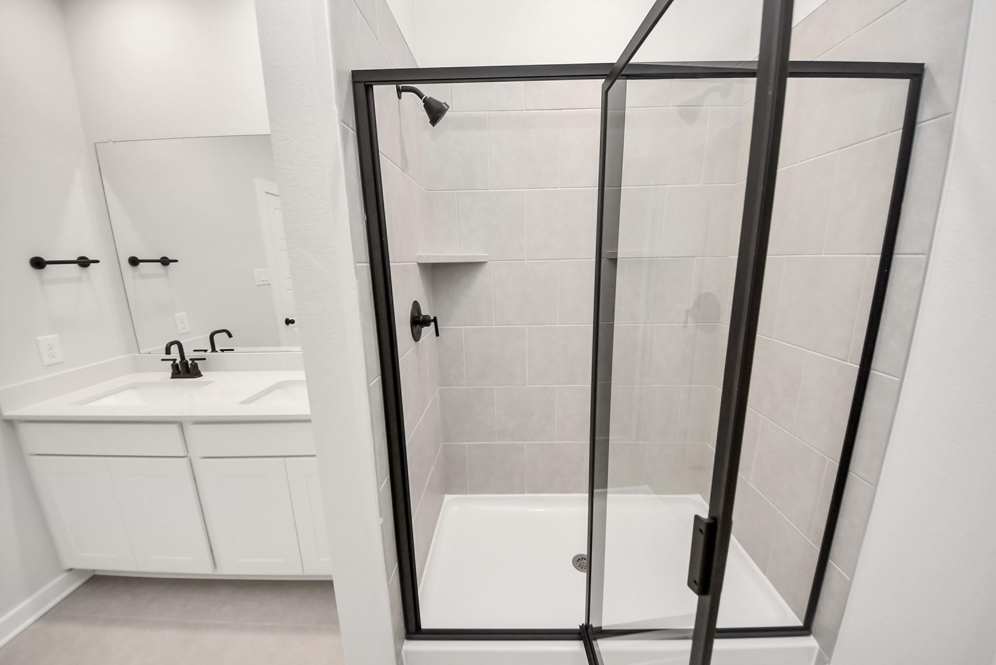 Modern bathroom with glass-enclosed shower and dual-sink vanity in The Daphne F by Davidson Homes, Sundance Cove, Crosby.