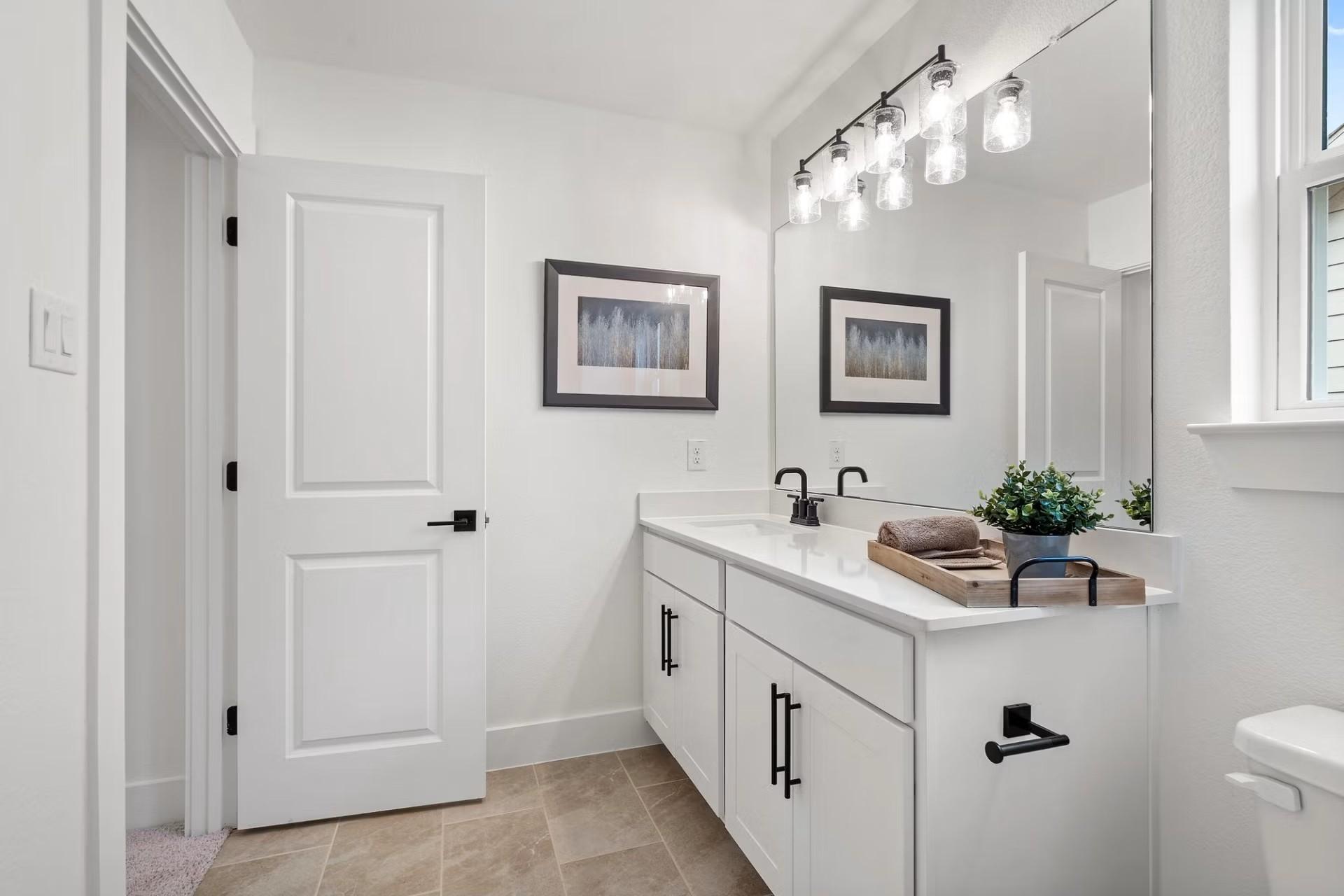 Bright powder room with white shaker vanity, chrome faucet, large frameless mirror, and pendant lights in The Wake D, Wylie Texas