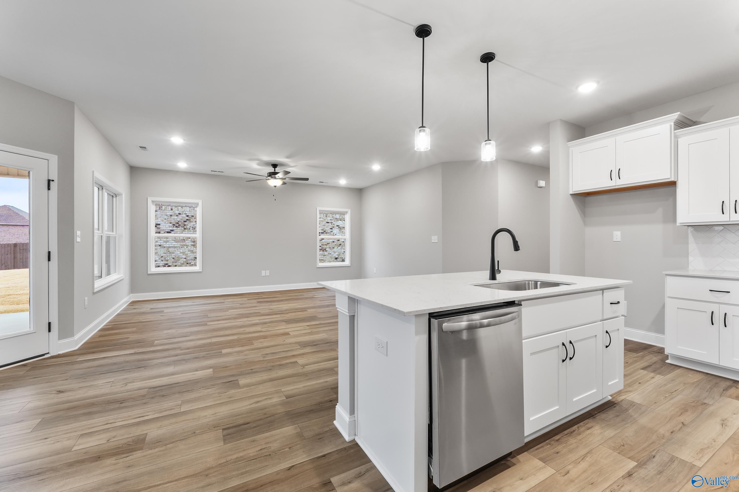 Modern open-concept kitchen with white shaker cabinets, quartz island, stainless dishwasher, and hardwood floors in The Asheville C home, Meridianville, Alabama
