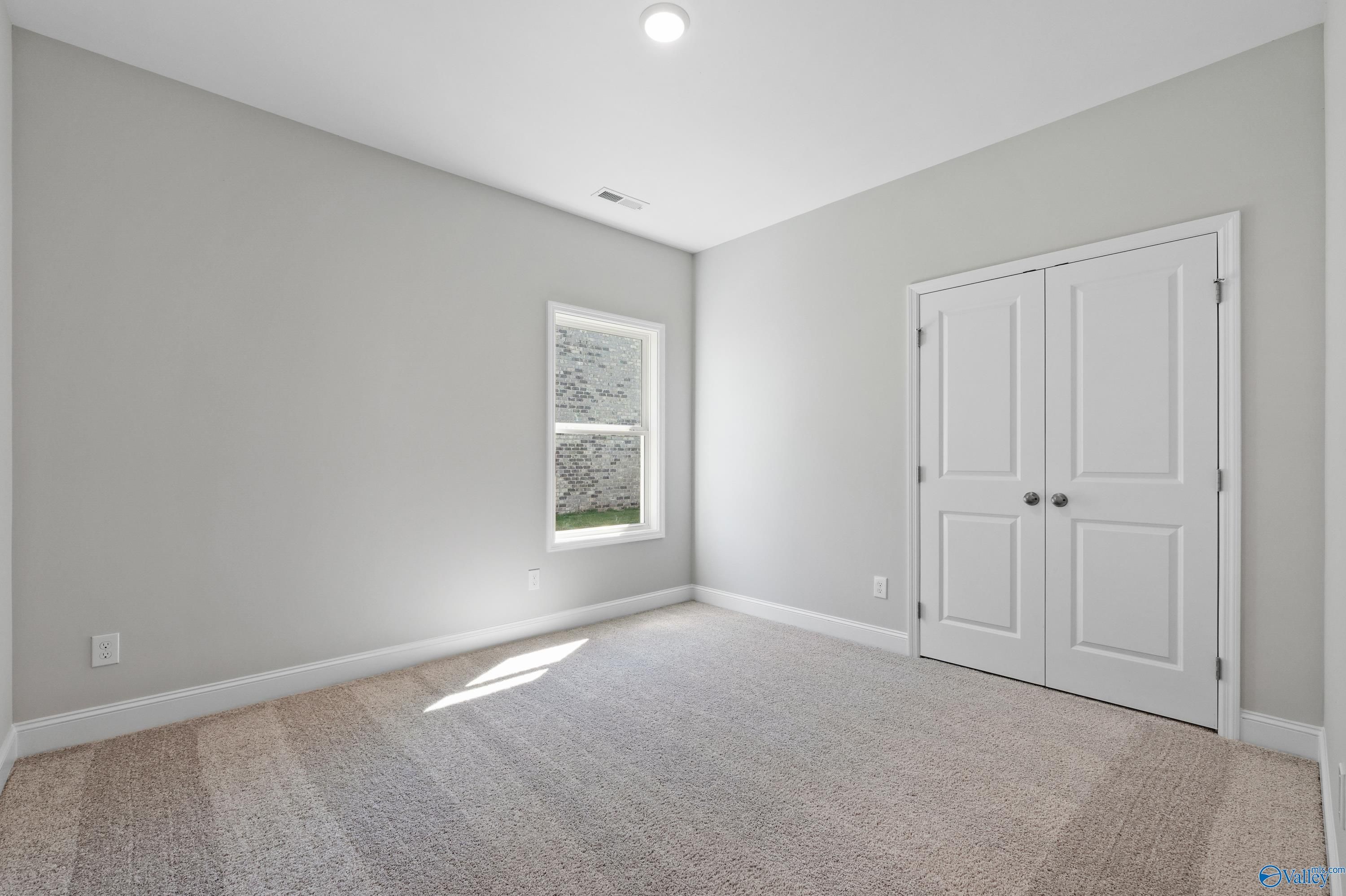 Empty bedroom with light gray walls, double doors, large window, and carpet in Davidson Homes The Everett, Hazel Green, AL