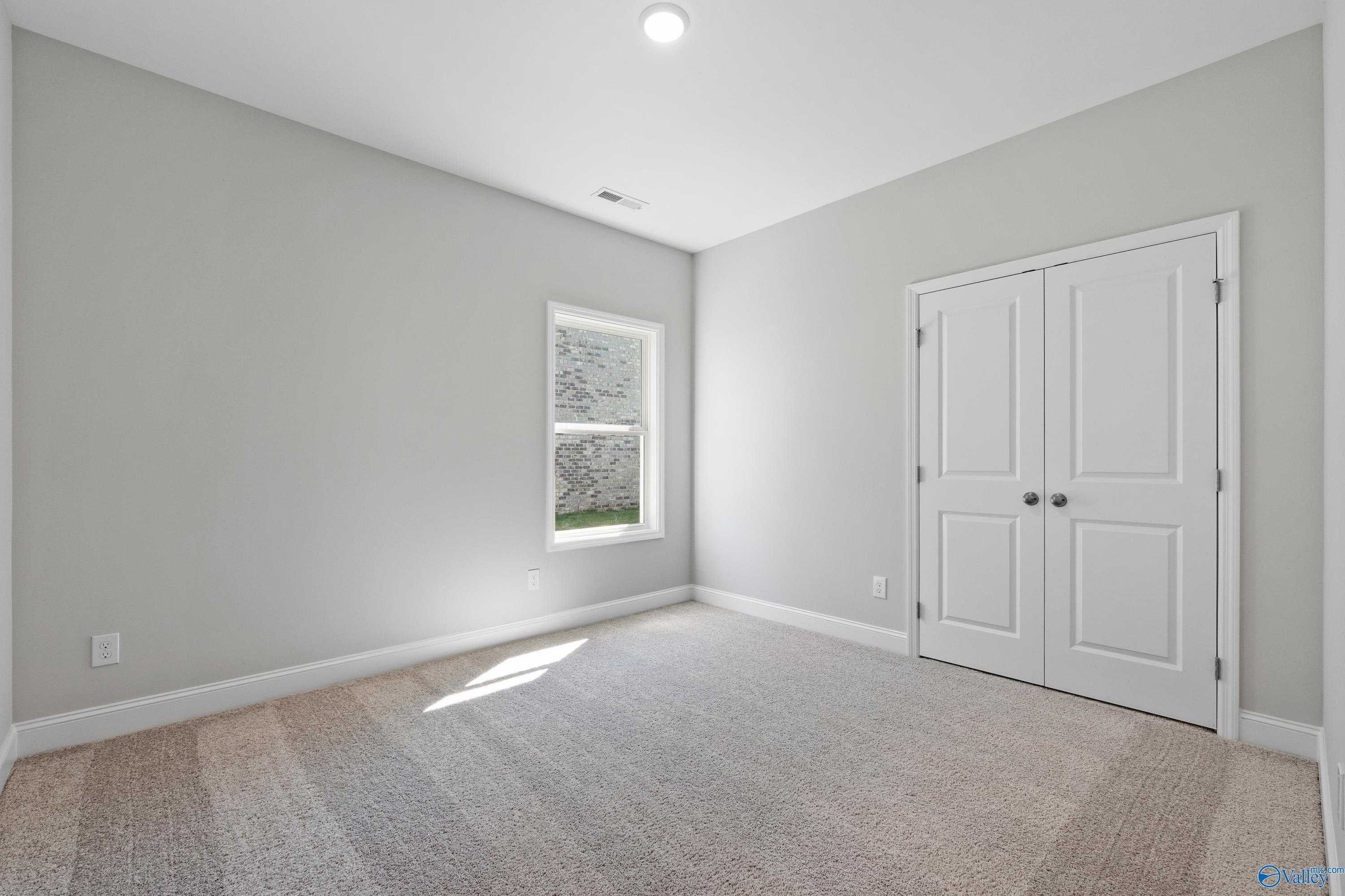 Empty bedroom with light gray walls, double doors, large window, and carpet in Davidson Homes The Everett, Hazel Green, AL