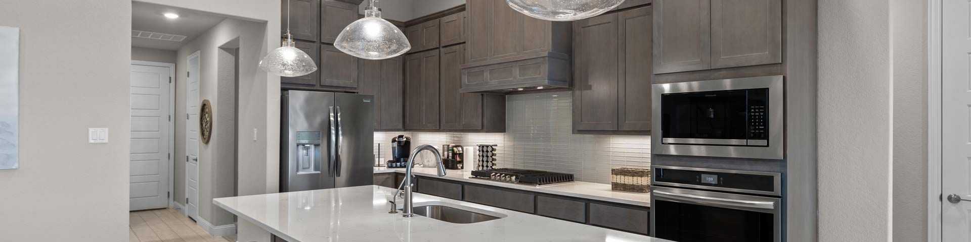 Modern kitchen with quartz island, gray shaker cabinets, and stainless appliances at The Reserve at Potranco Oaks in Castroville, Texas