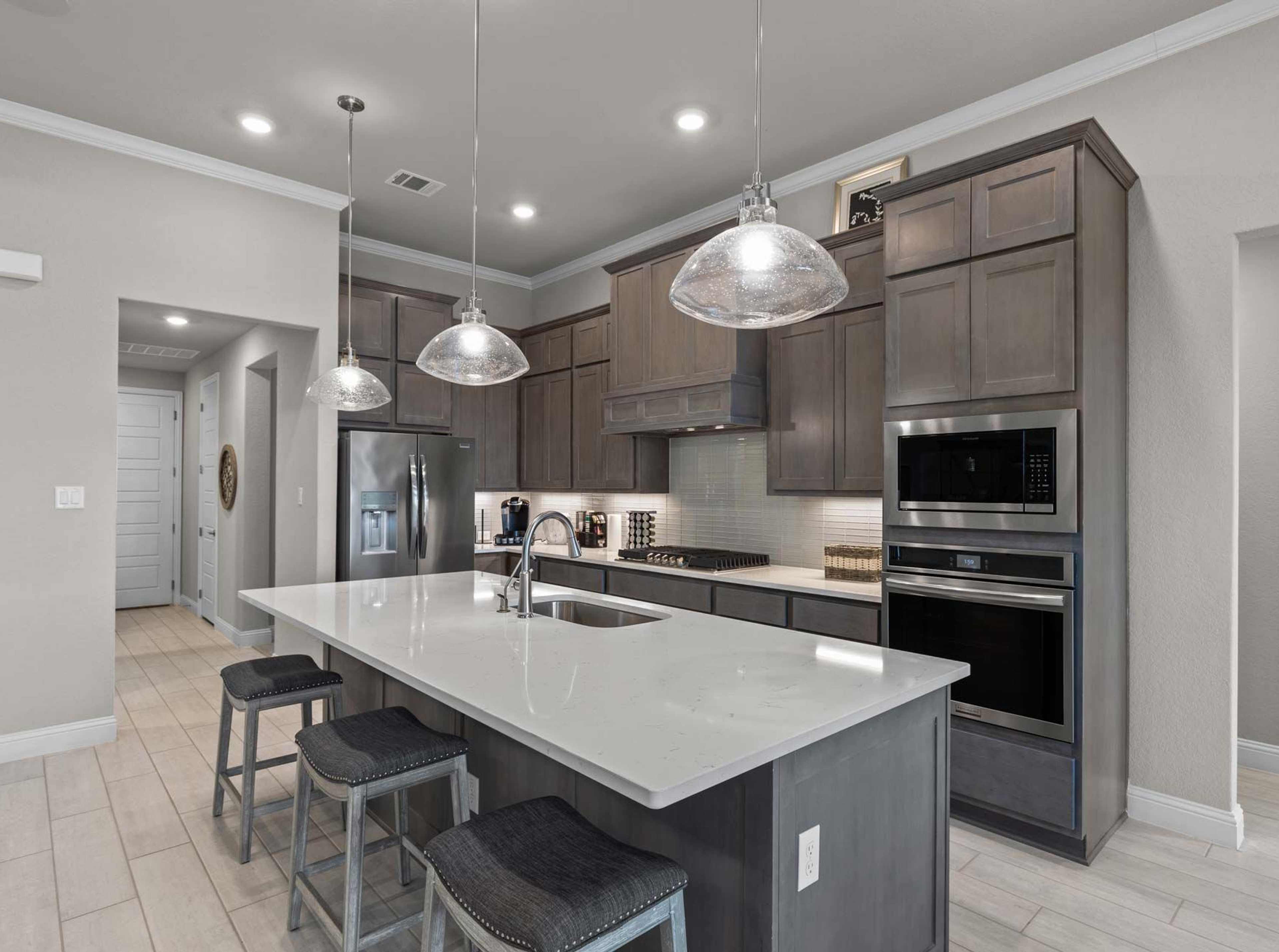Modern kitchen with quartz island, gray shaker cabinets, and stainless appliances at The Reserve at Potranco Oaks in Castroville, Texas
