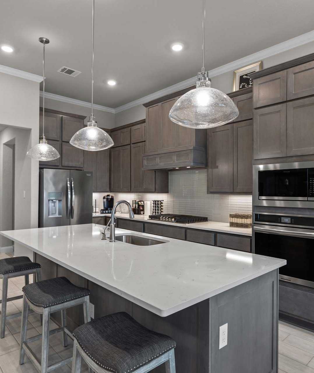 Modern kitchen with quartz island, gray shaker cabinets, and stainless appliances at The Reserve at Potranco Oaks in Castroville, Texas