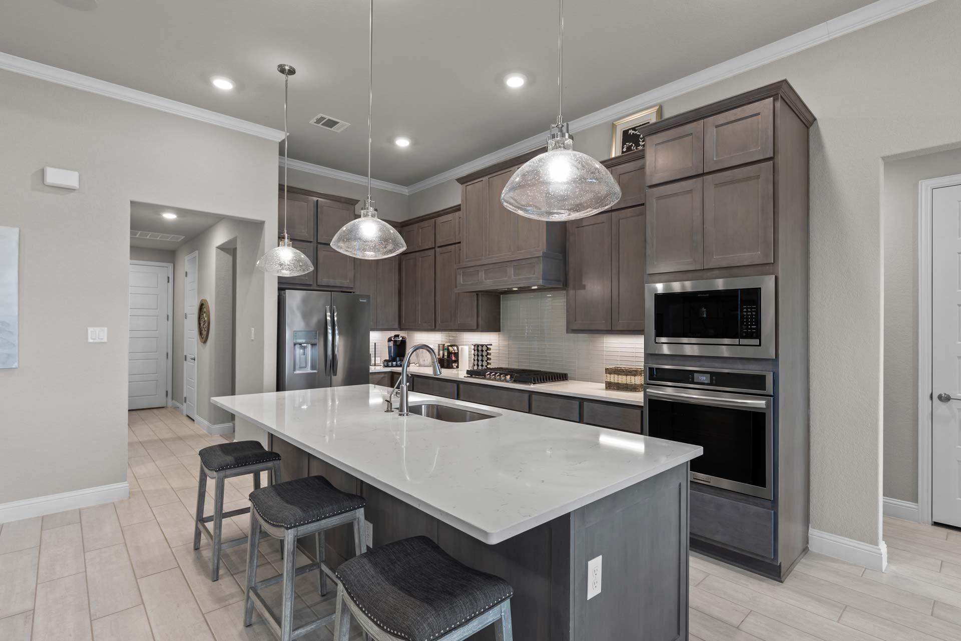 Modern kitchen with quartz island, gray shaker cabinets, and stainless appliances at The Reserve at Potranco Oaks in Castroville, Texas