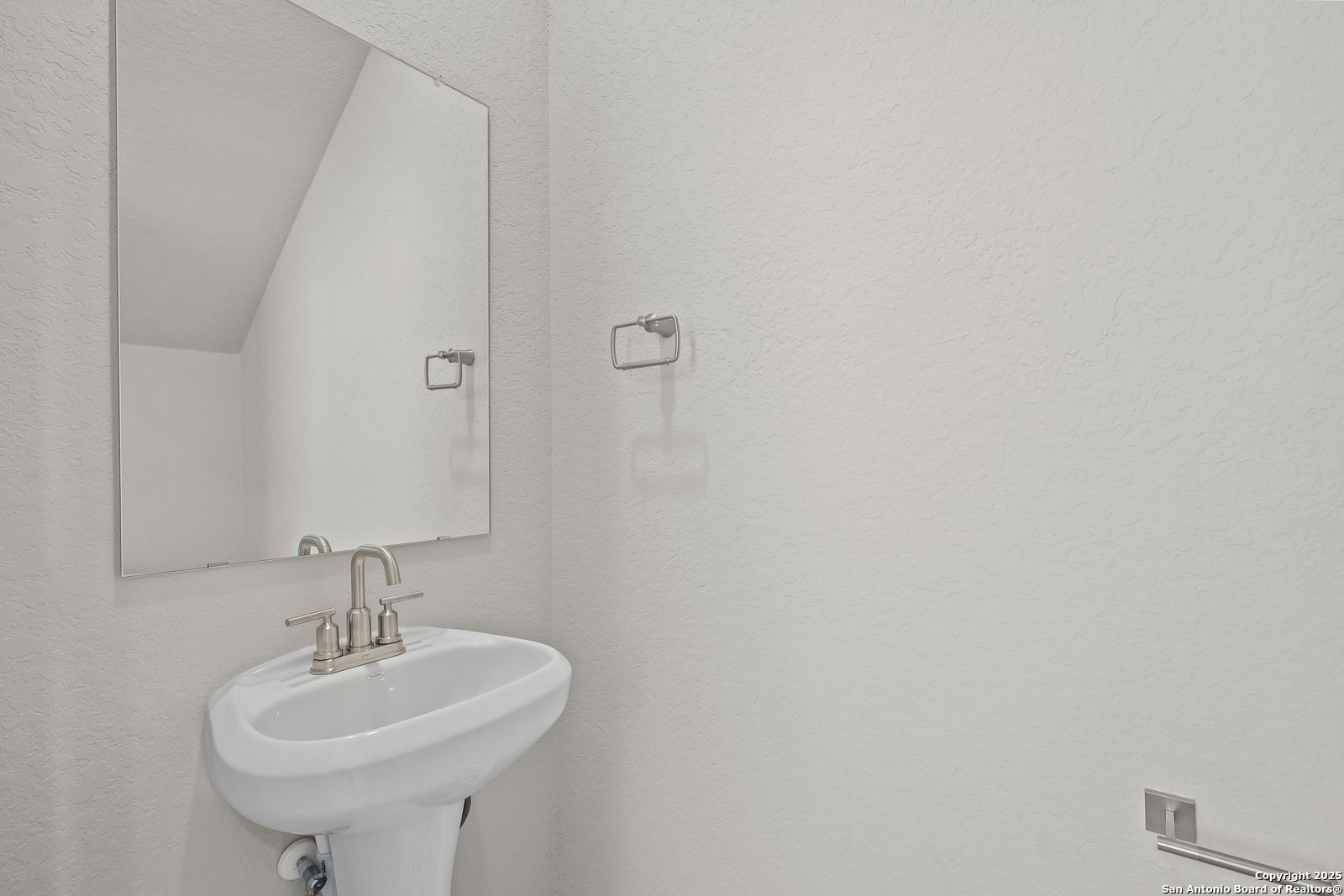 White pedestal sink with chrome faucet under large mirror in powder room of Davidson Homes The Trinity D, Applewhite Meadows, San Antonio