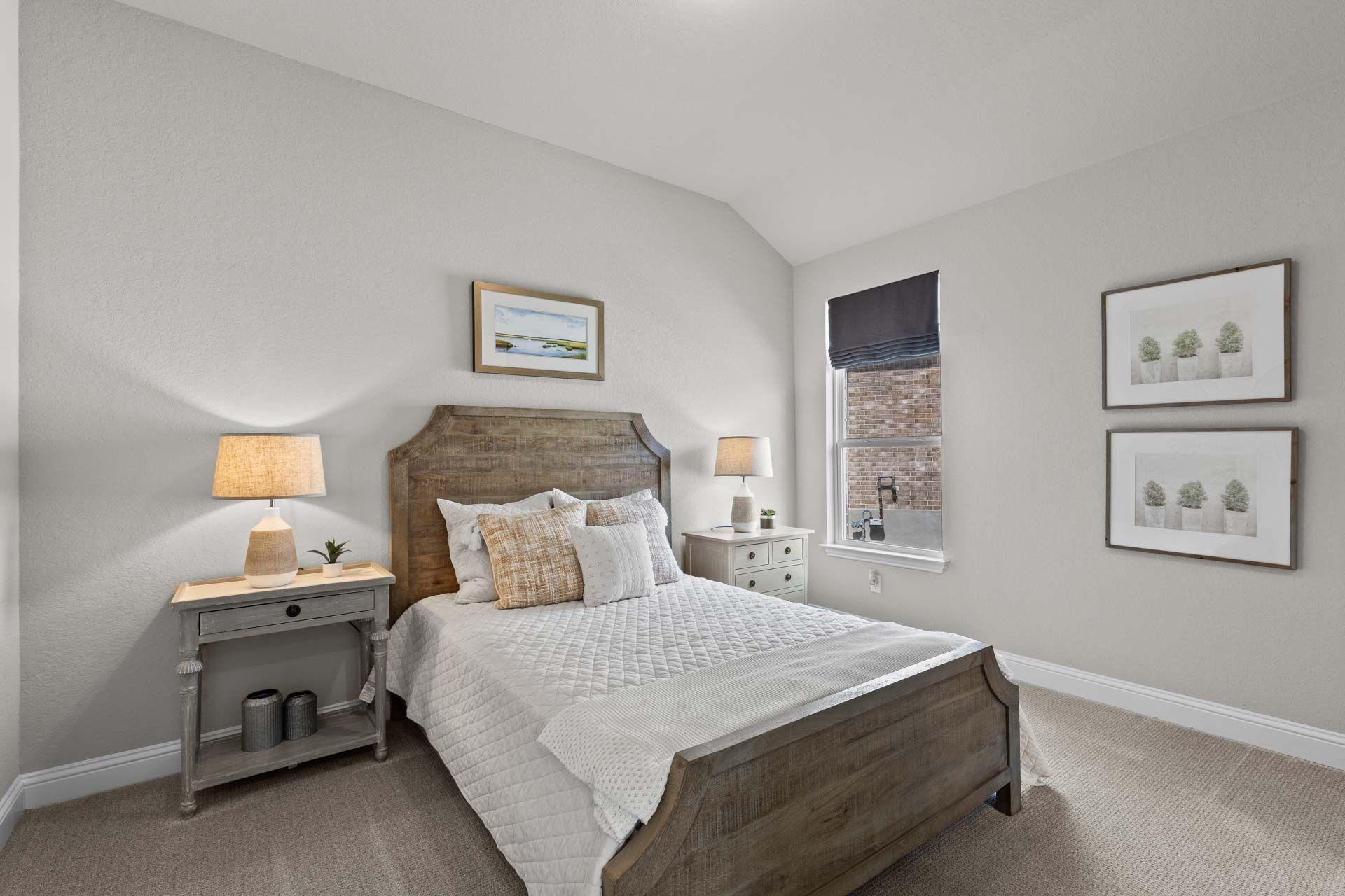 Cozy bedroom at Ladera in San Antonio Texas with wooden bed frame, white bedding, orange pillows, and neutral gray walls