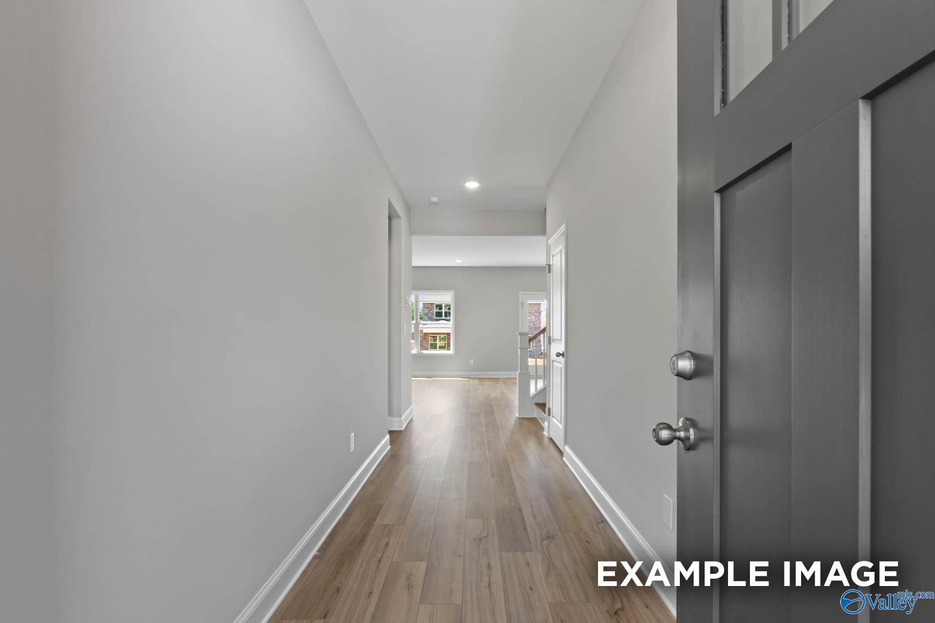 Spacious entry hallway with light gray walls, hardwood floors, and dark gray front door in Davidson Homes The Chelsea B, New Market, Alabama
