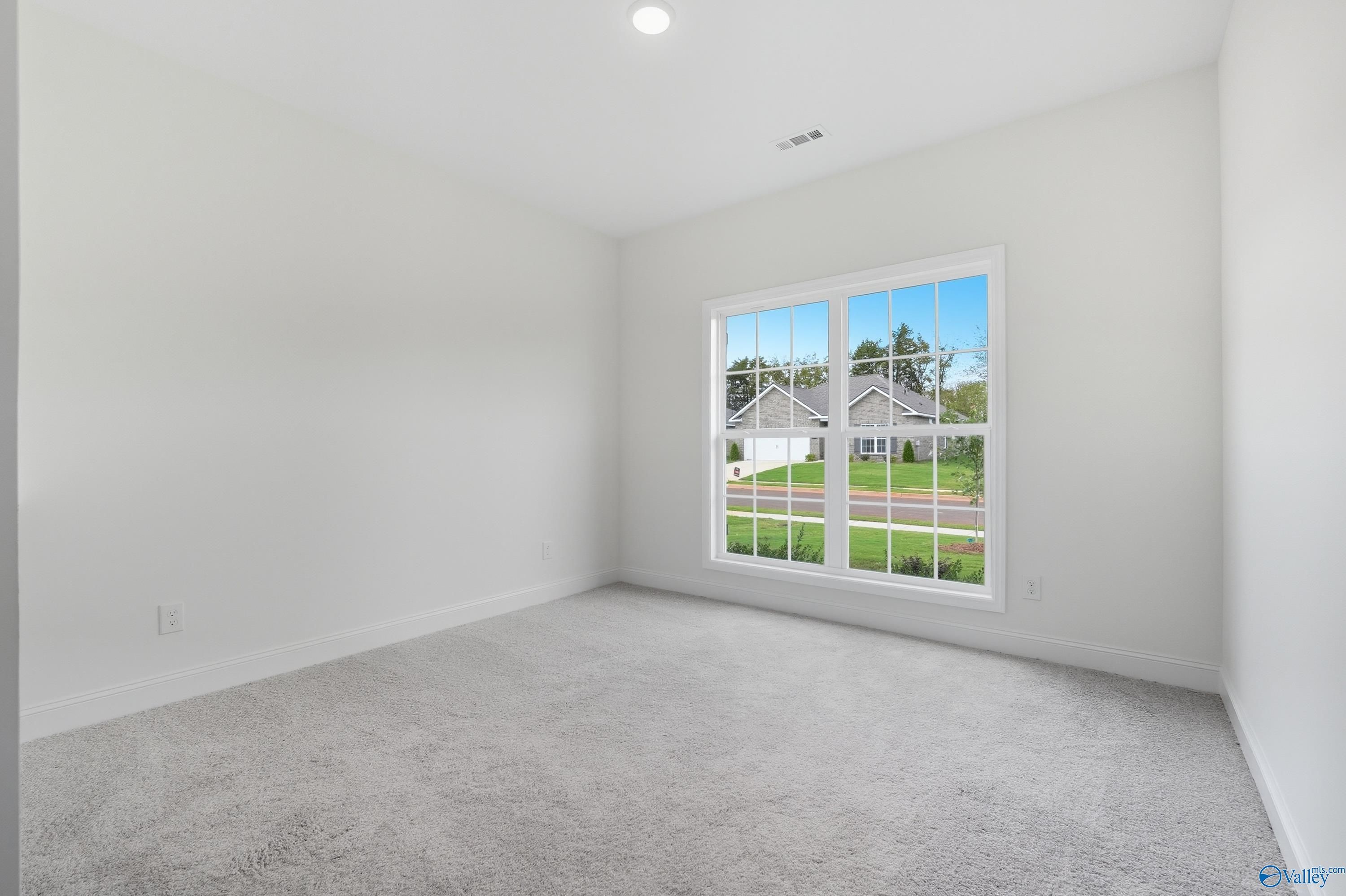 Bright empty bedroom with large window view of neighborhood, white walls, gray carpet in Davidson Homes The Everett, Meridianville, AL