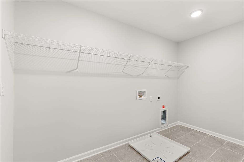 Spacious laundry room with wire shelving, washer-dryer hookups, and tiled floor in Davidson Homes The Hickory B, Winder, Georgia