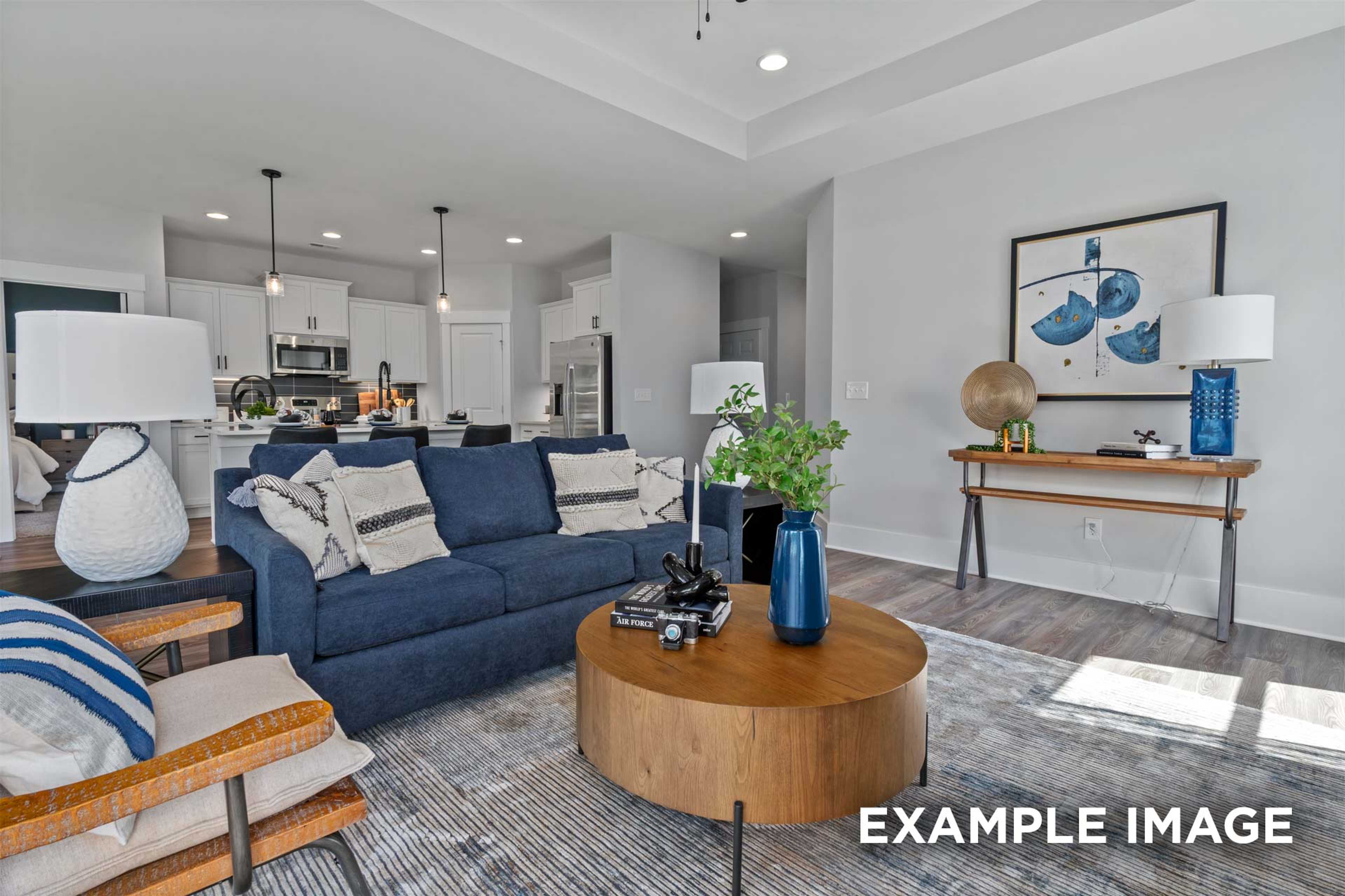 Spacious open-concept living room in The Franklin C Davidson Homes, Lillington NC, featuring navy sofa, wood coffee table, and modern kitchen