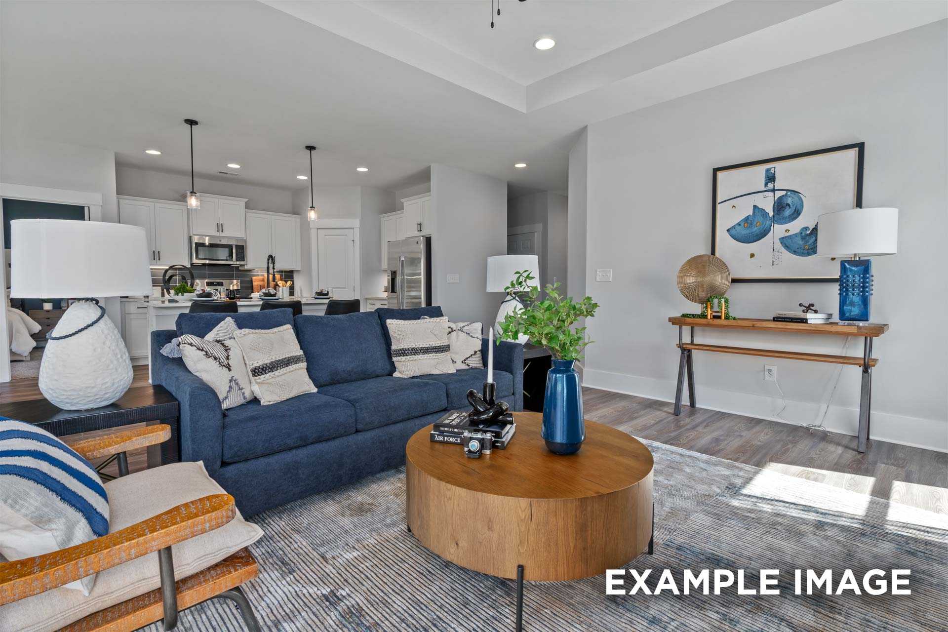 Spacious open-concept living room in The Franklin C Davidson Homes, Lillington NC, featuring navy sofa, wood coffee table, and modern kitchen