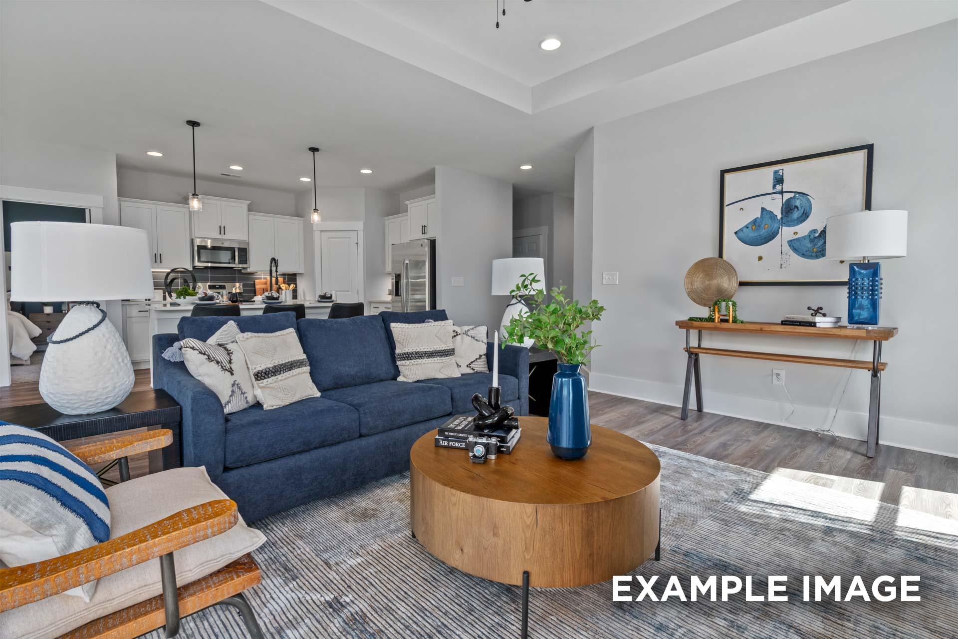 Spacious open-concept living room in The Franklin C Davidson Homes, Lillington NC, featuring navy sofa, wood coffee table, and modern kitchen