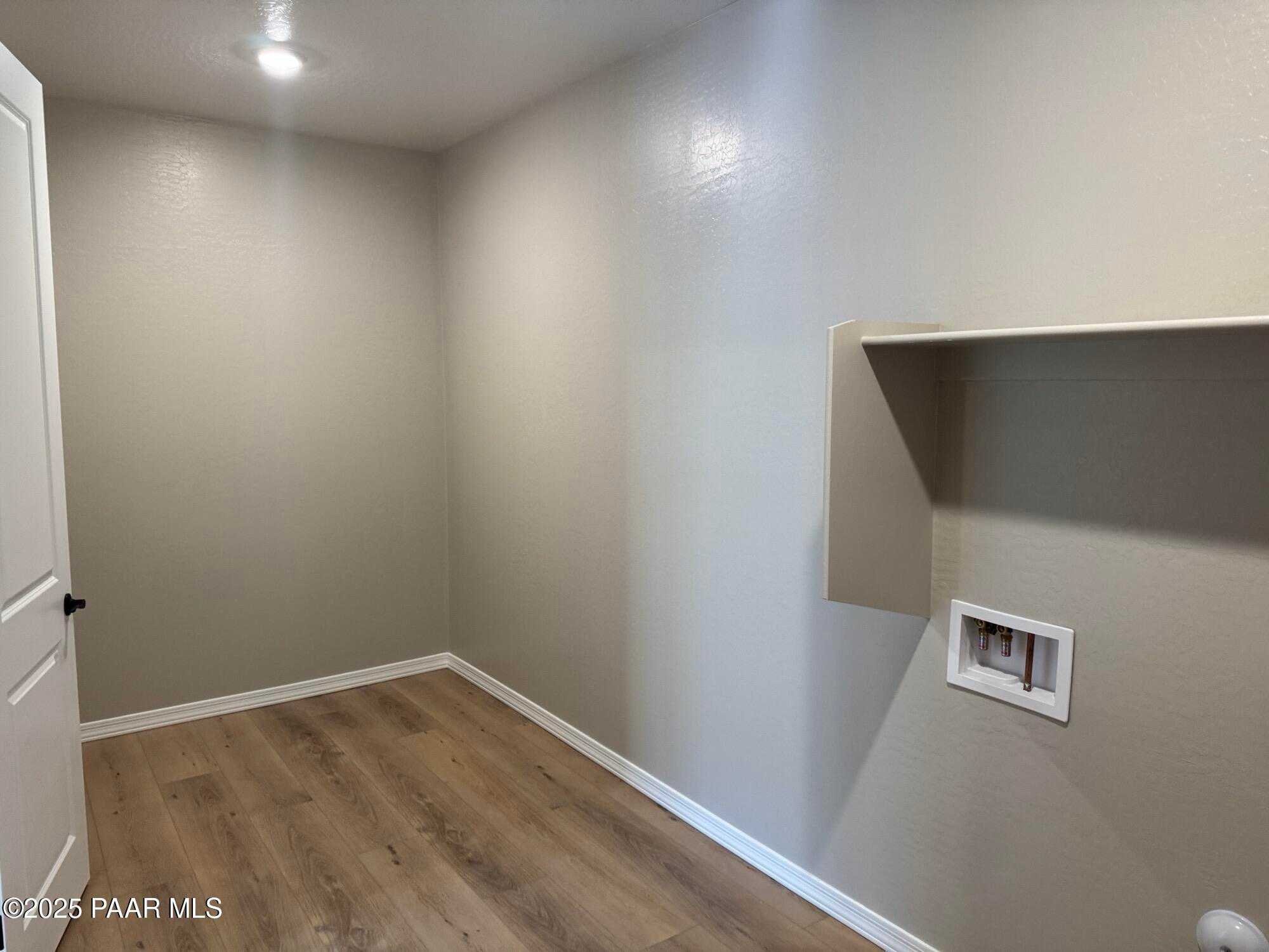 Bright laundry room with beige walls, wood laminate flooring, built-in shelf, and utility hookups in Davidson Homes The Sheridan II B, Prescott AZ