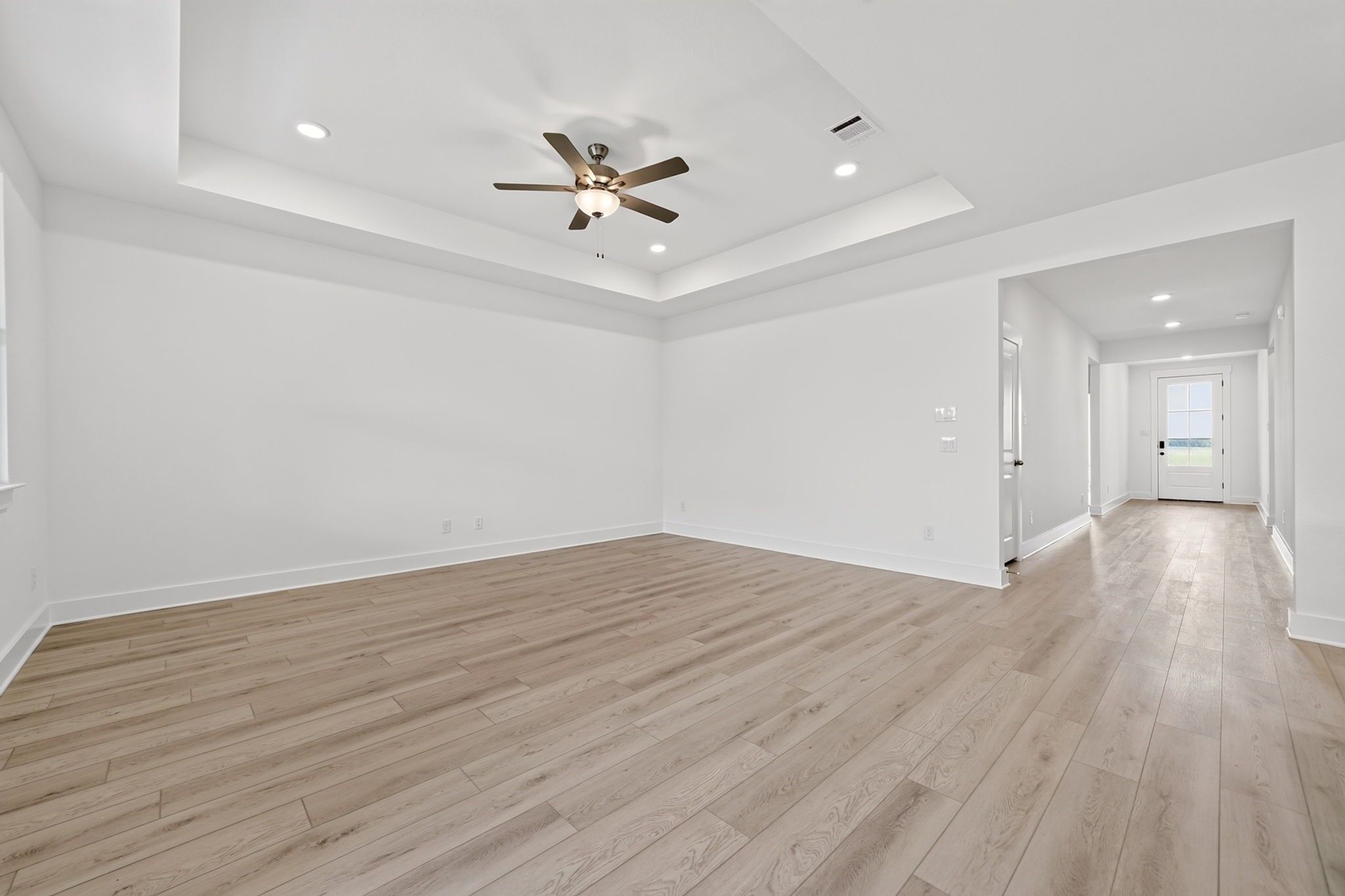 Bright open-concept living room with tray ceiling, ceiling fan, and luxury vinyl plank flooring in Davidson Homes Holly F plan, Josephine TX