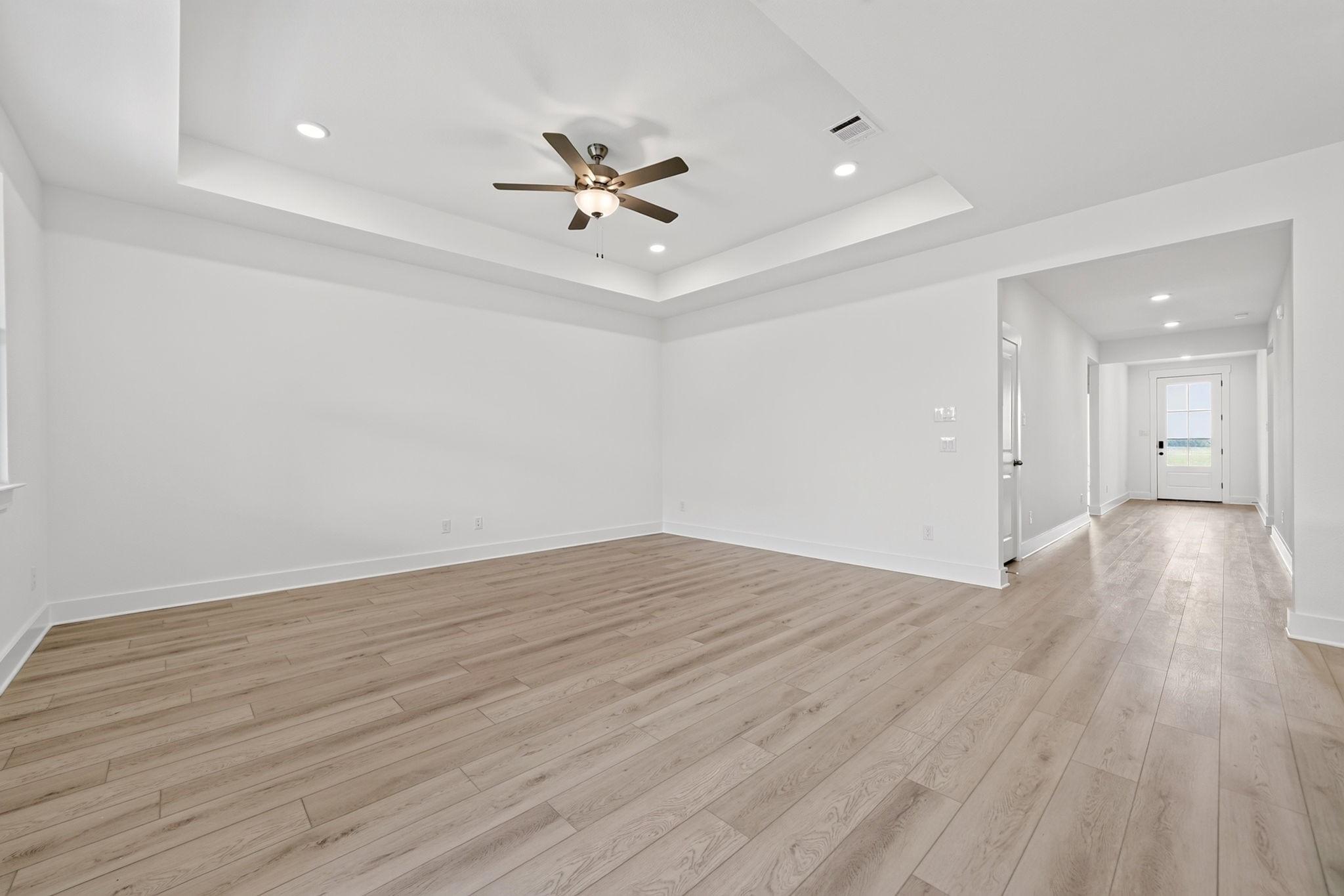 Bright open-concept living room with tray ceiling, ceiling fan, and luxury vinyl plank flooring in Davidson Homes Holly F plan, Josephine TX