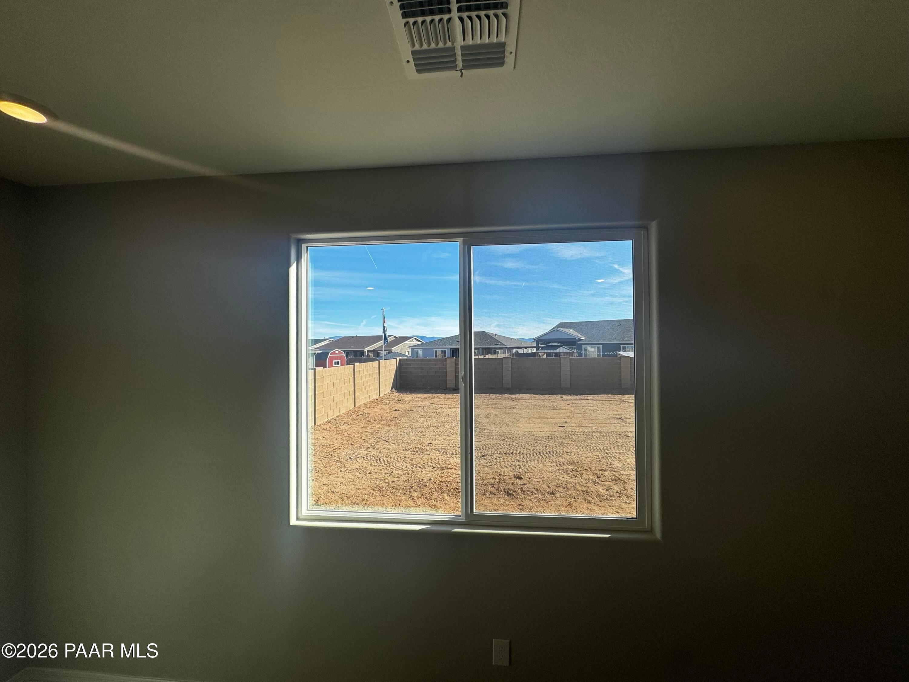 Bright empty room with large window overlooking fenced dirt yard and distant homes in Davidson Homes Daybreak B, Prescott AZ