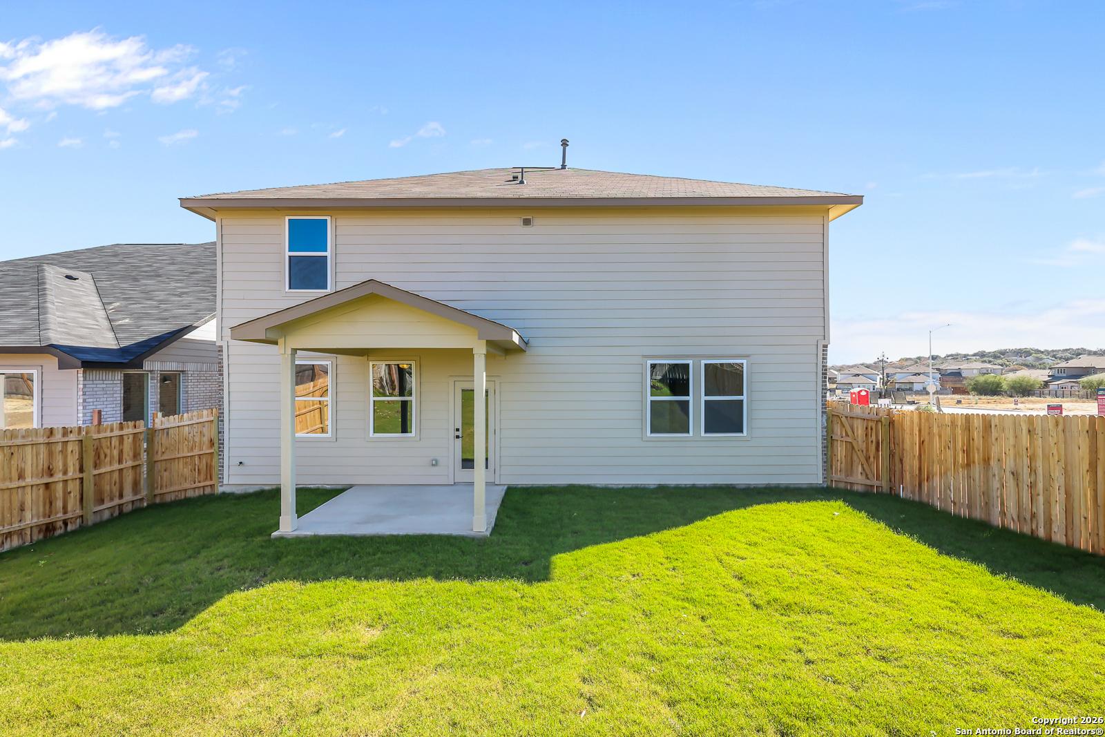 Two-story beige home with covered back patio, large windows, and fenced grassy yard in Comanche Ridge, San Antonio, Texas - Davidson Homes Douglas E