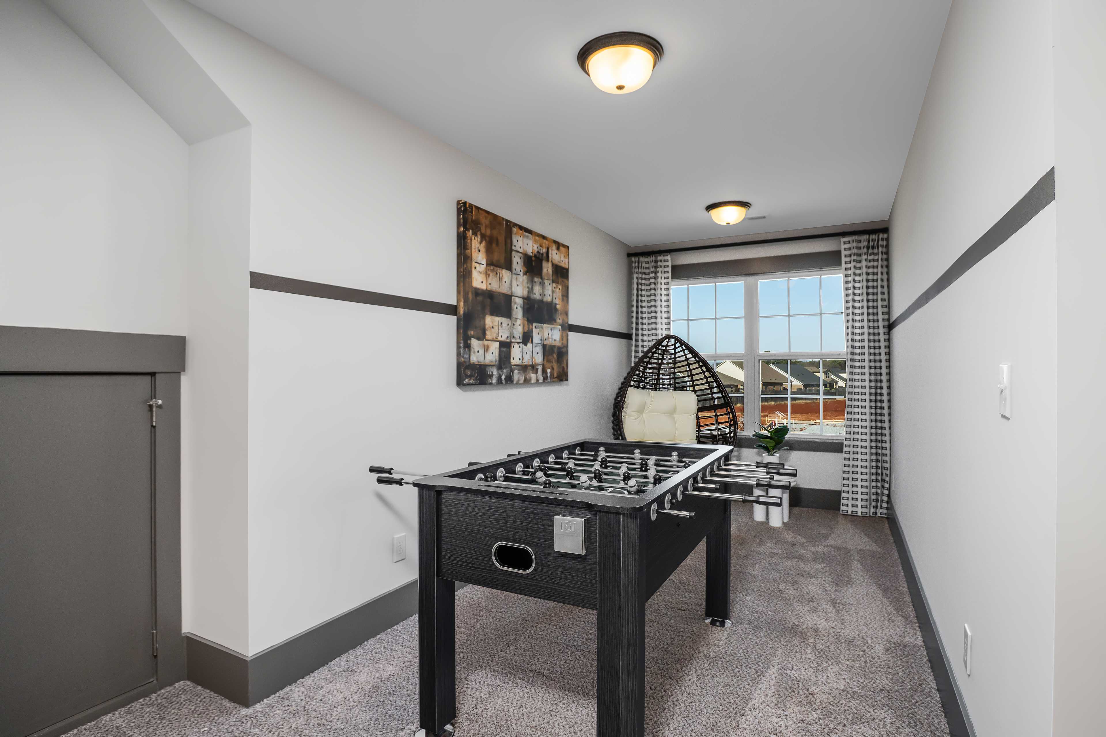 Bonus room at Barnett's Crossing in Madison Alabama with black foosball table, wicker chair, and abstract art