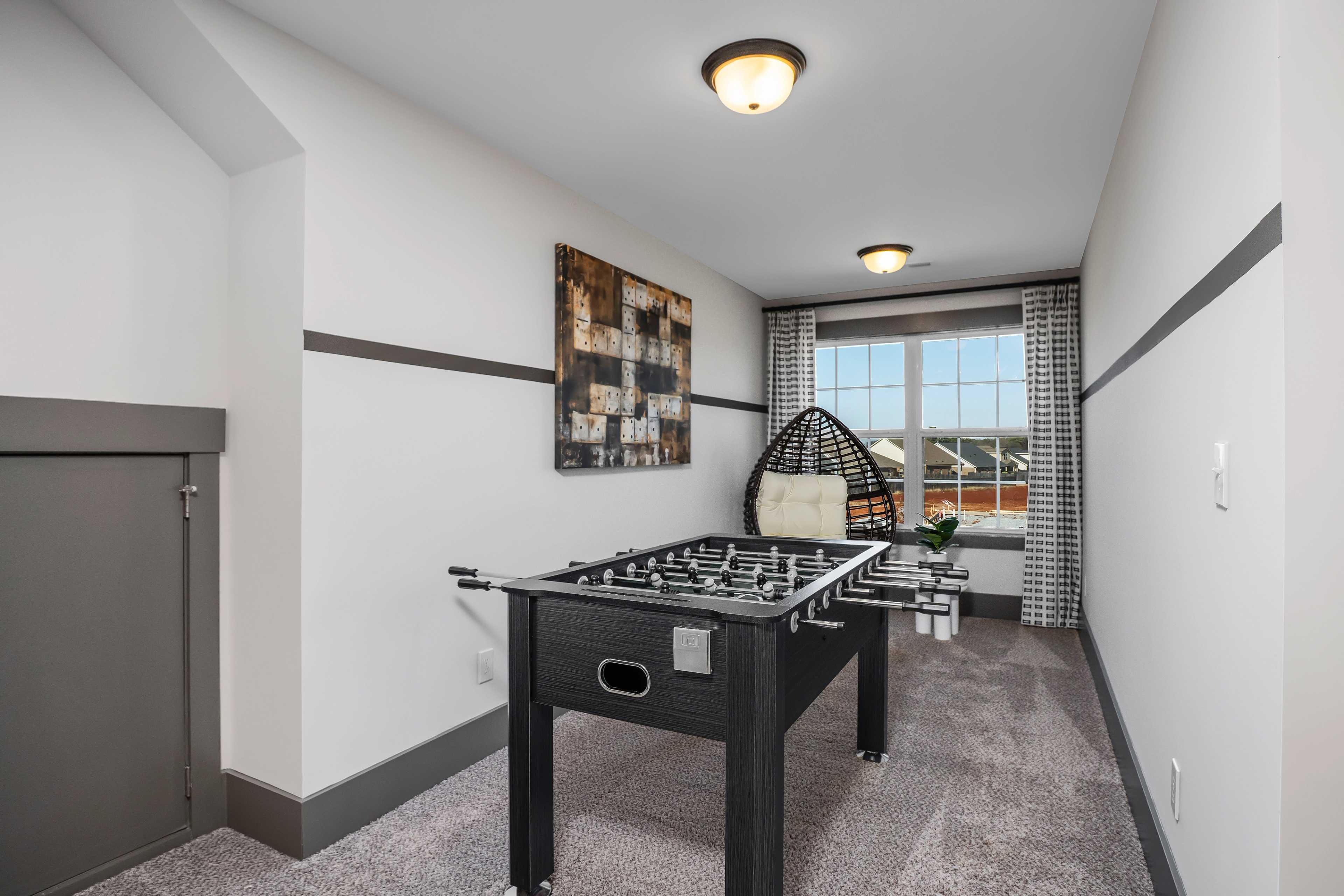 Bonus room at Barnett's Crossing in Madison Alabama with black foosball table, wicker chair, and abstract art