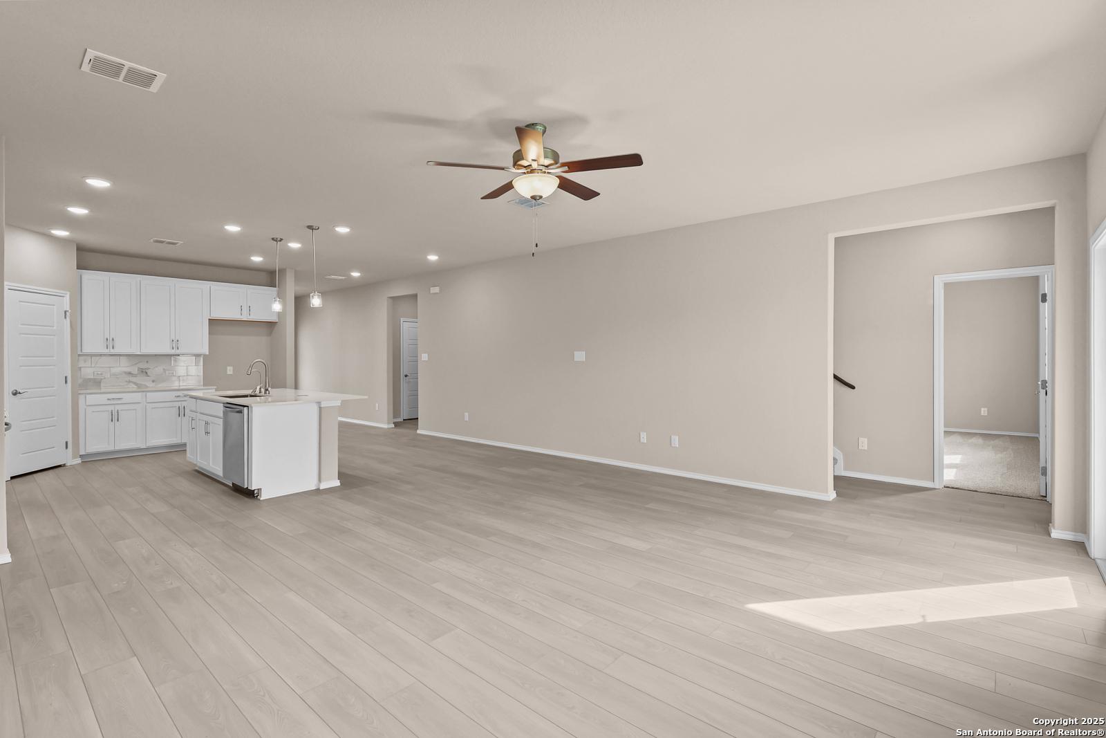 Open kitchen with white cabinets, center island sink, ceiling fan, and light wood floors in Davidson Homes The Douglas G, San Antonio