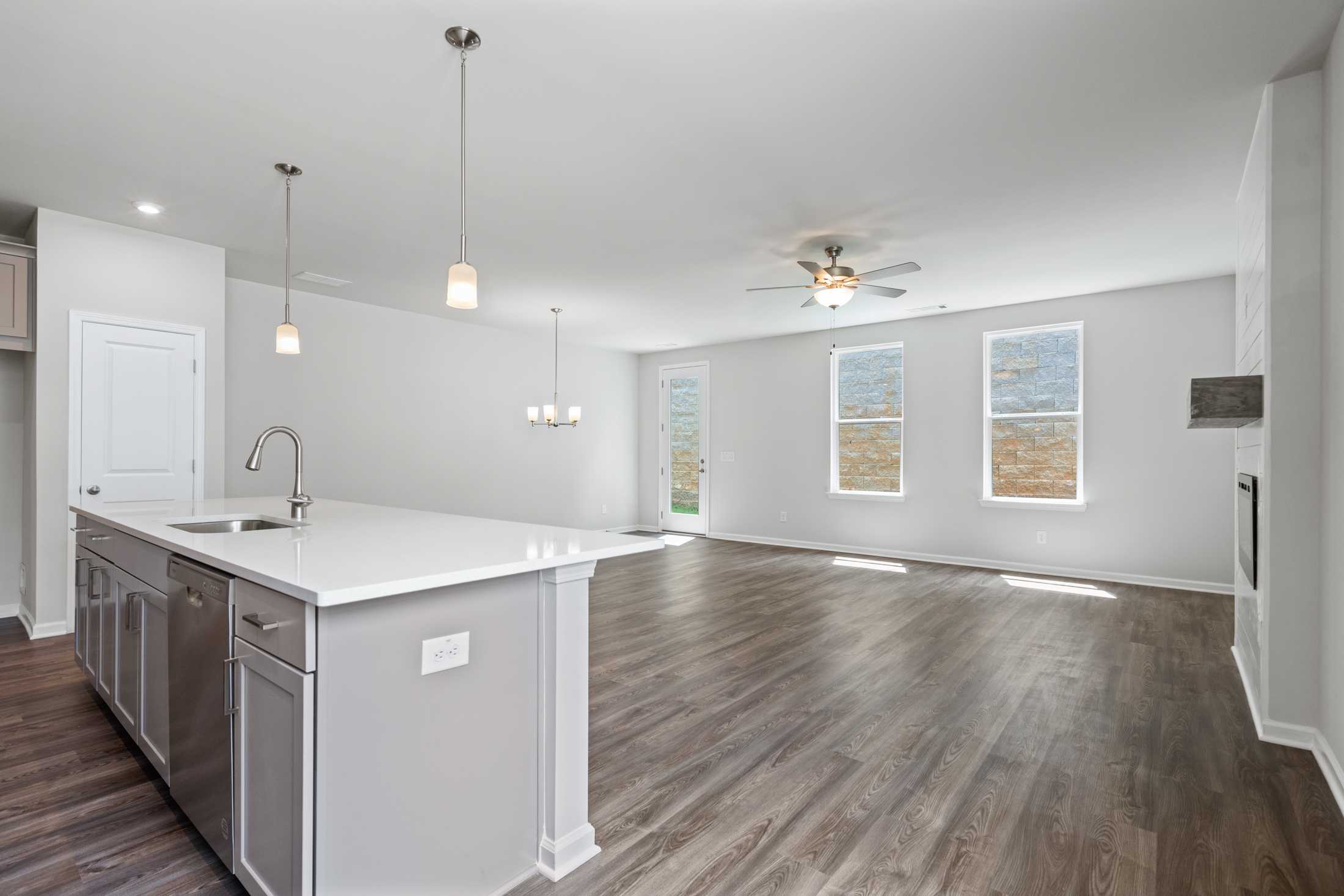 Open-concept kitchen in The Cary A home featuring white shaker cabinets, large quartz island with sink, hardwood floors, and large sunny windows